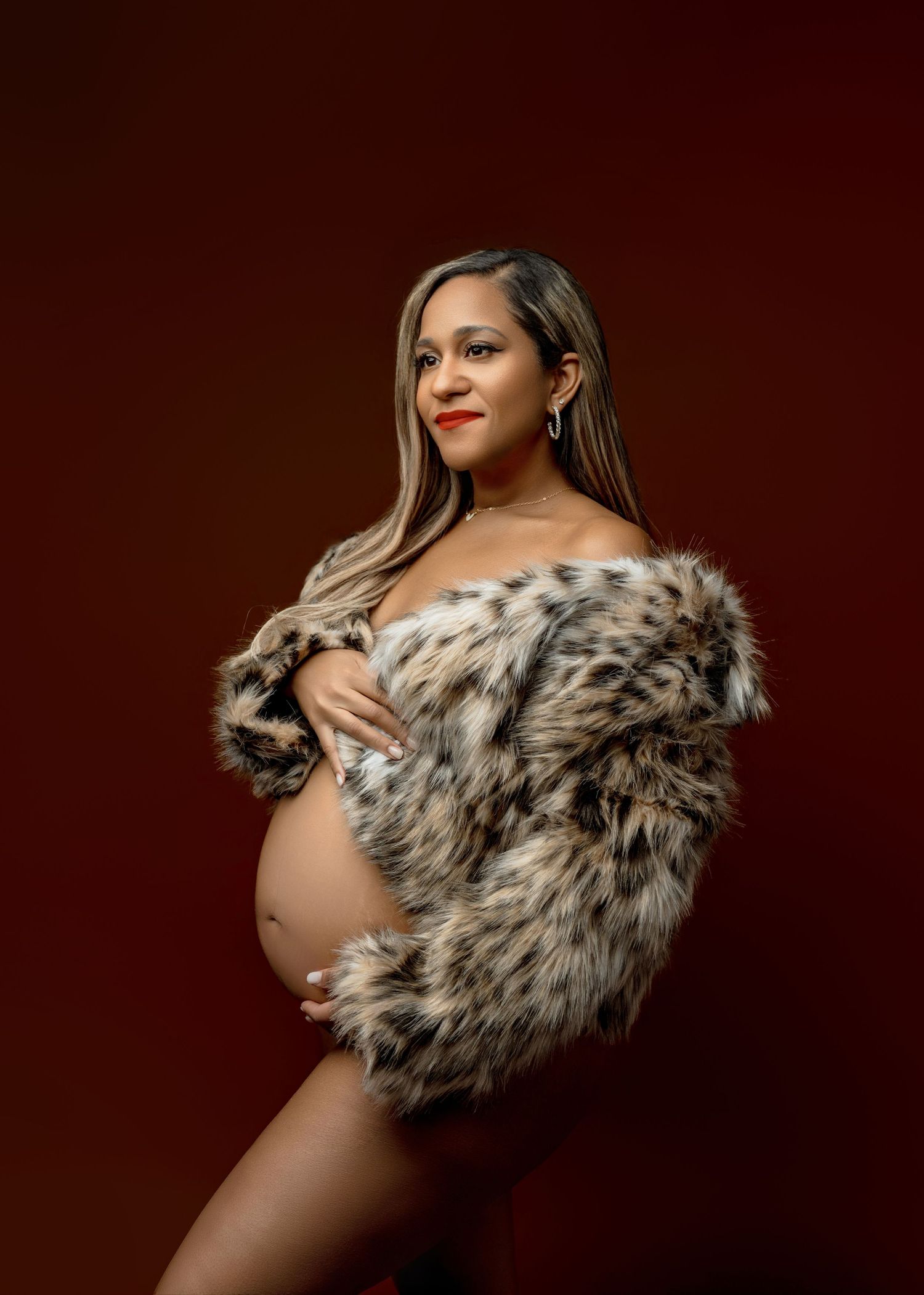 A maternity photoshoot featuring a spotted faux fur wrap against a dark brown background.