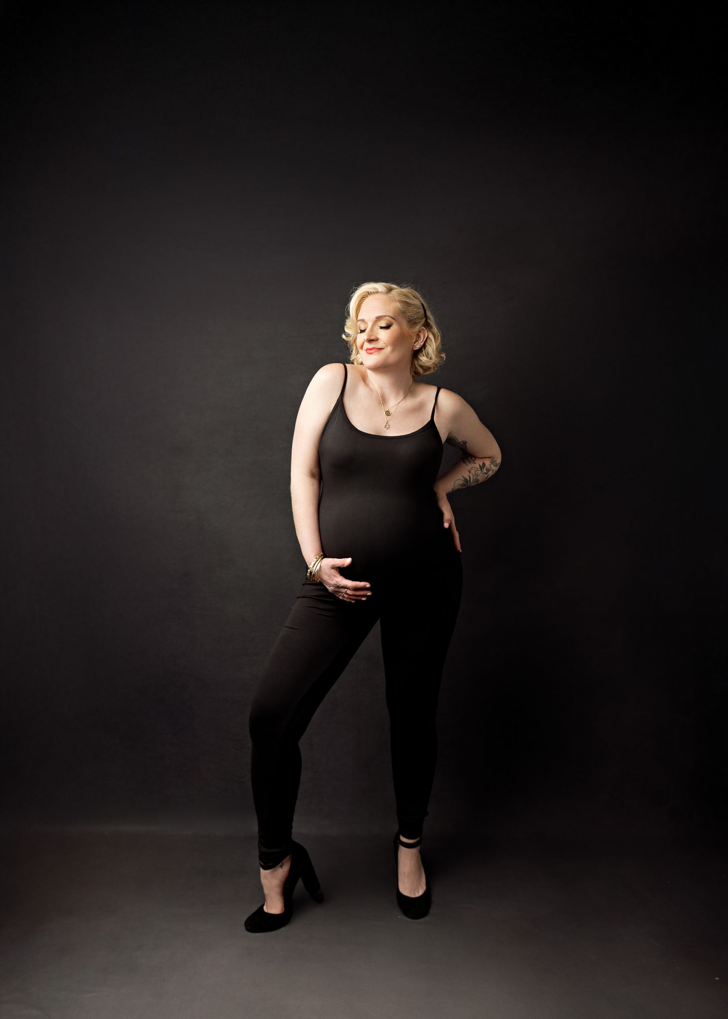 A figure in a black tank top and leggings strikes a confident pose against a dark studio backdrop.