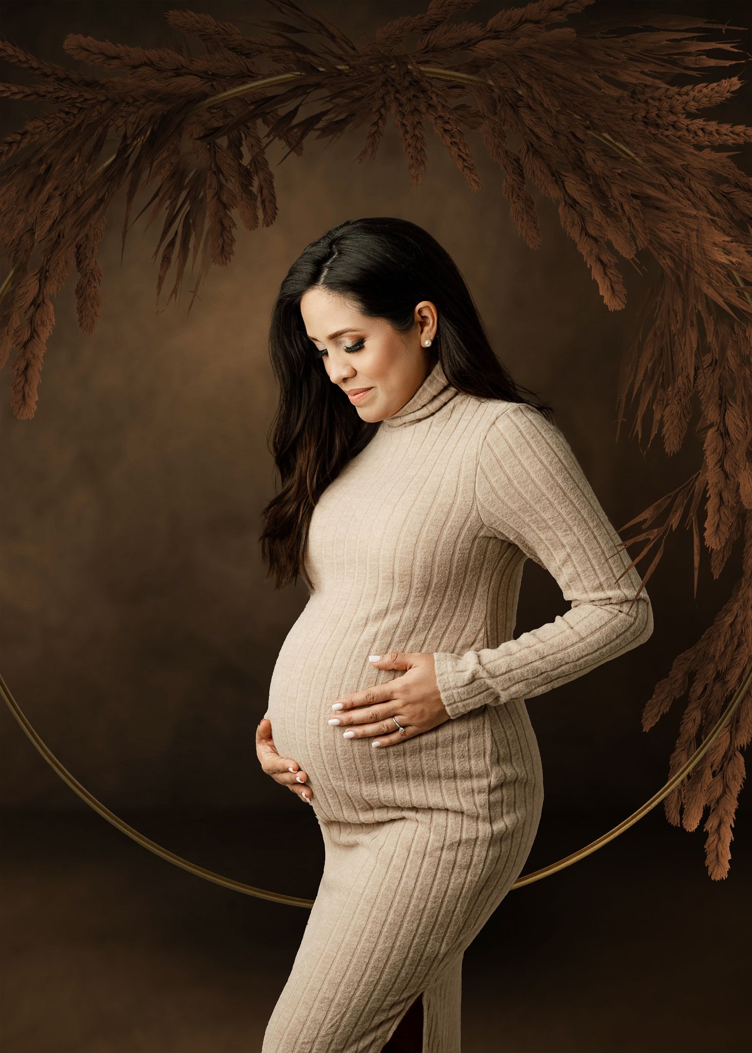 Artistic maternity portrait with beige ribbed dress against dark background with dried palm fronds and circular frame.