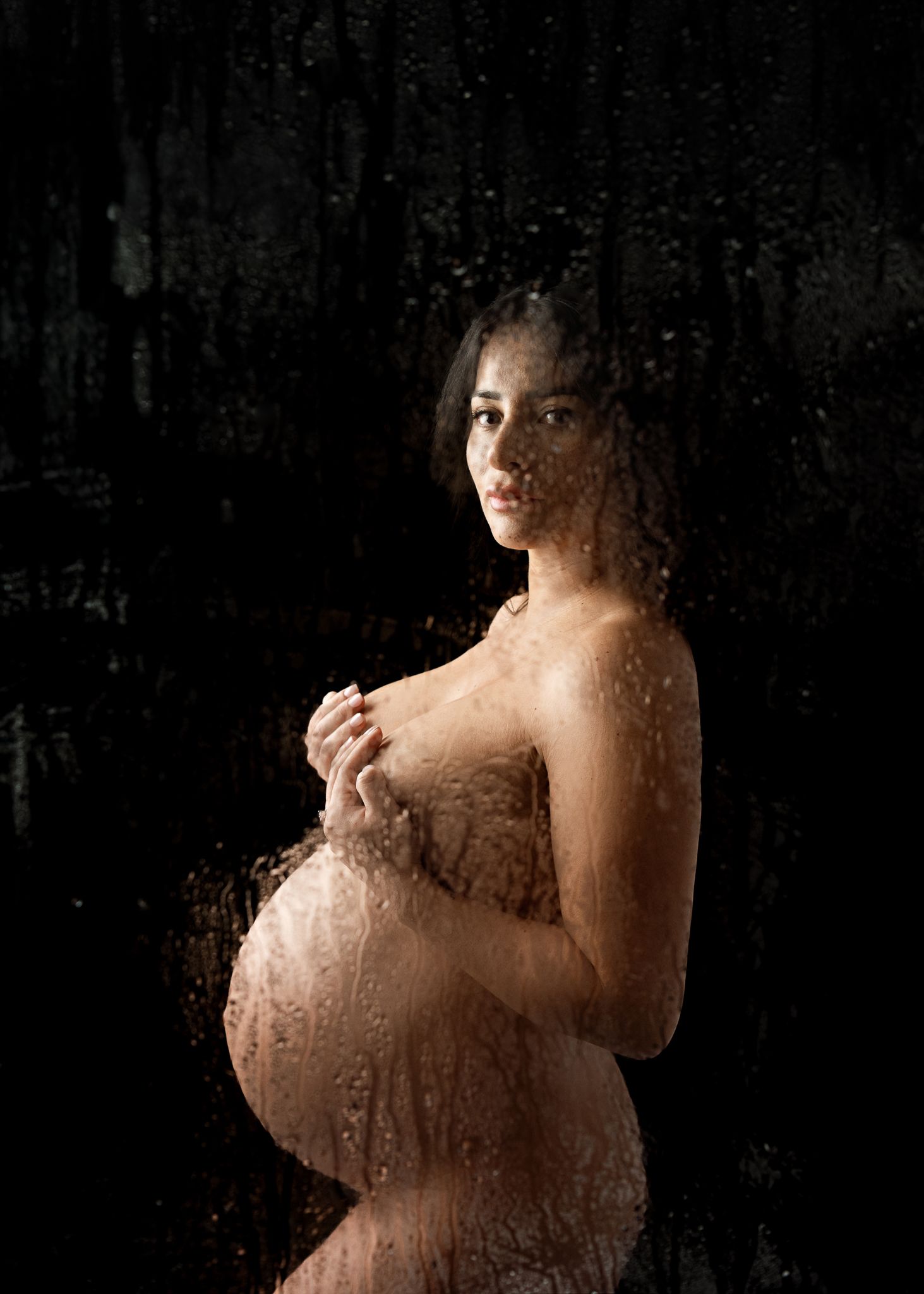 Artistic maternity portrait featuring water droplets and dramatic lighting against a dark backdrop.