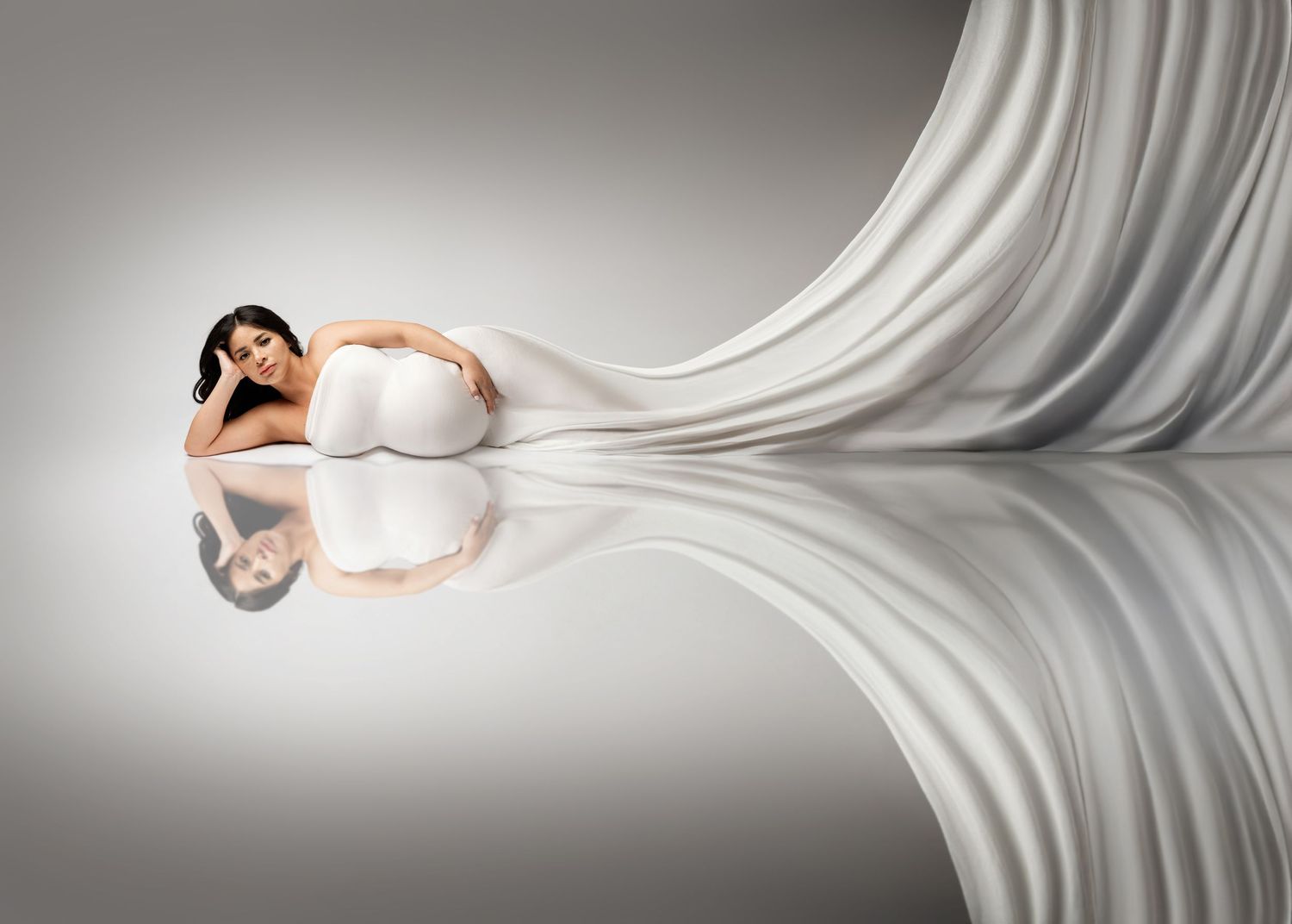 Elegant maternity photo with flowing white fabric creating dramatic reflection on glossy surface on Long Island, NY