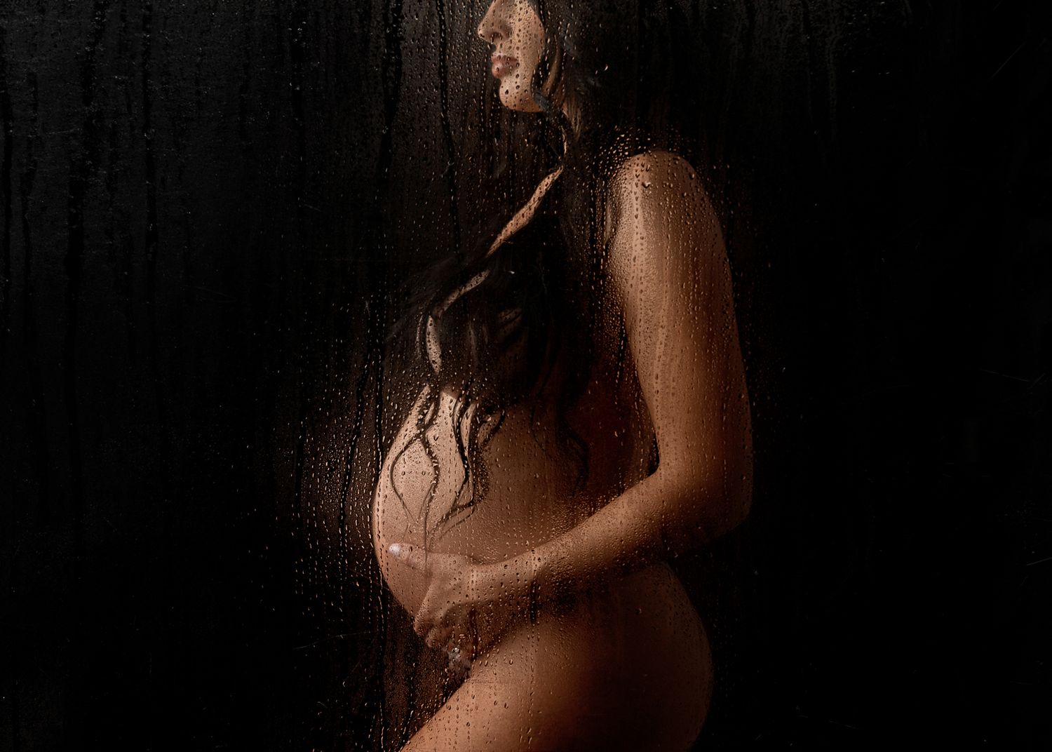 Dramatic silhouette of expectant mother in dark moody lighting with water droplet effects.