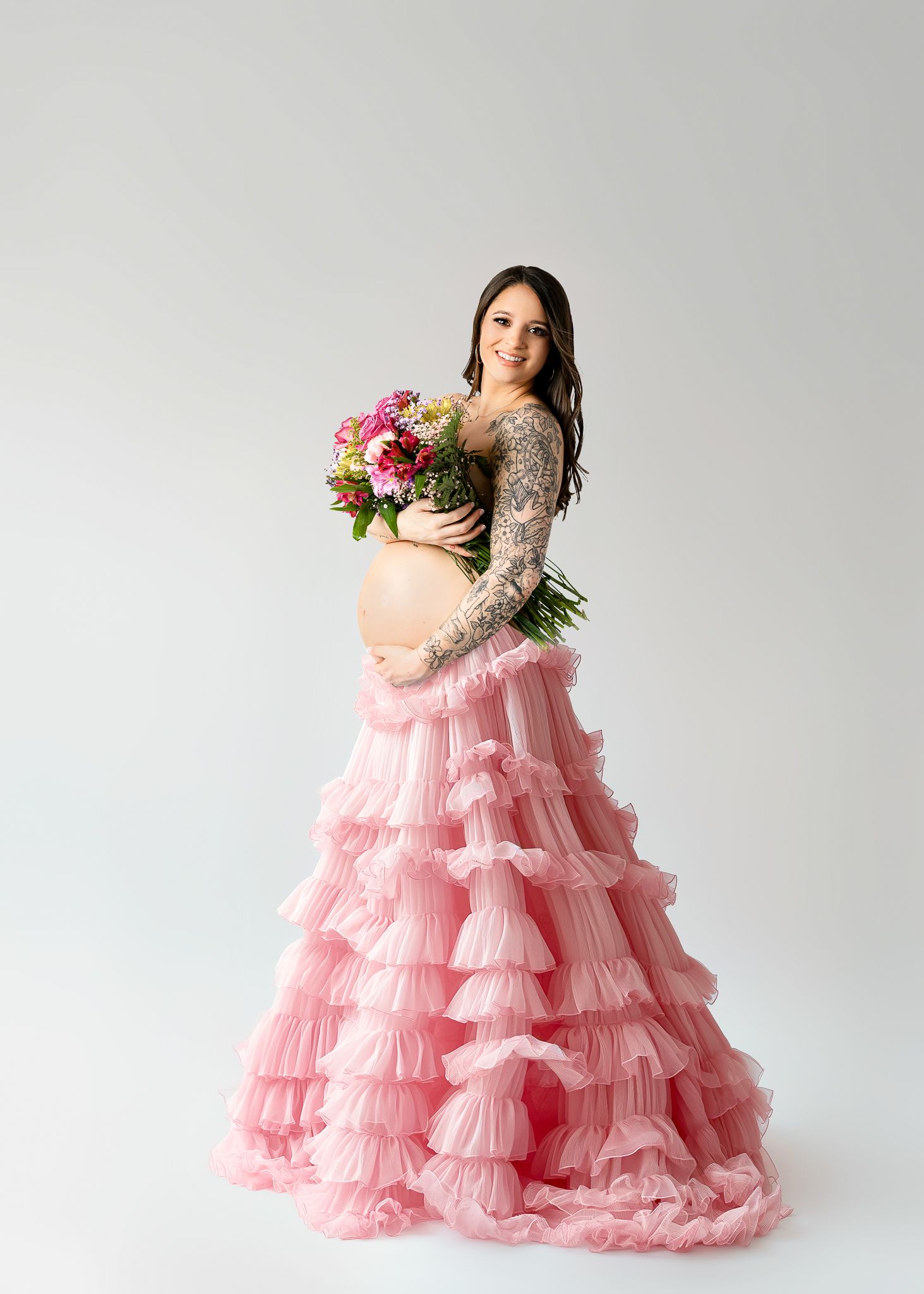 Maternity portrait featuring a pink tiered tulle skirt, lace top and colorful bouquet.