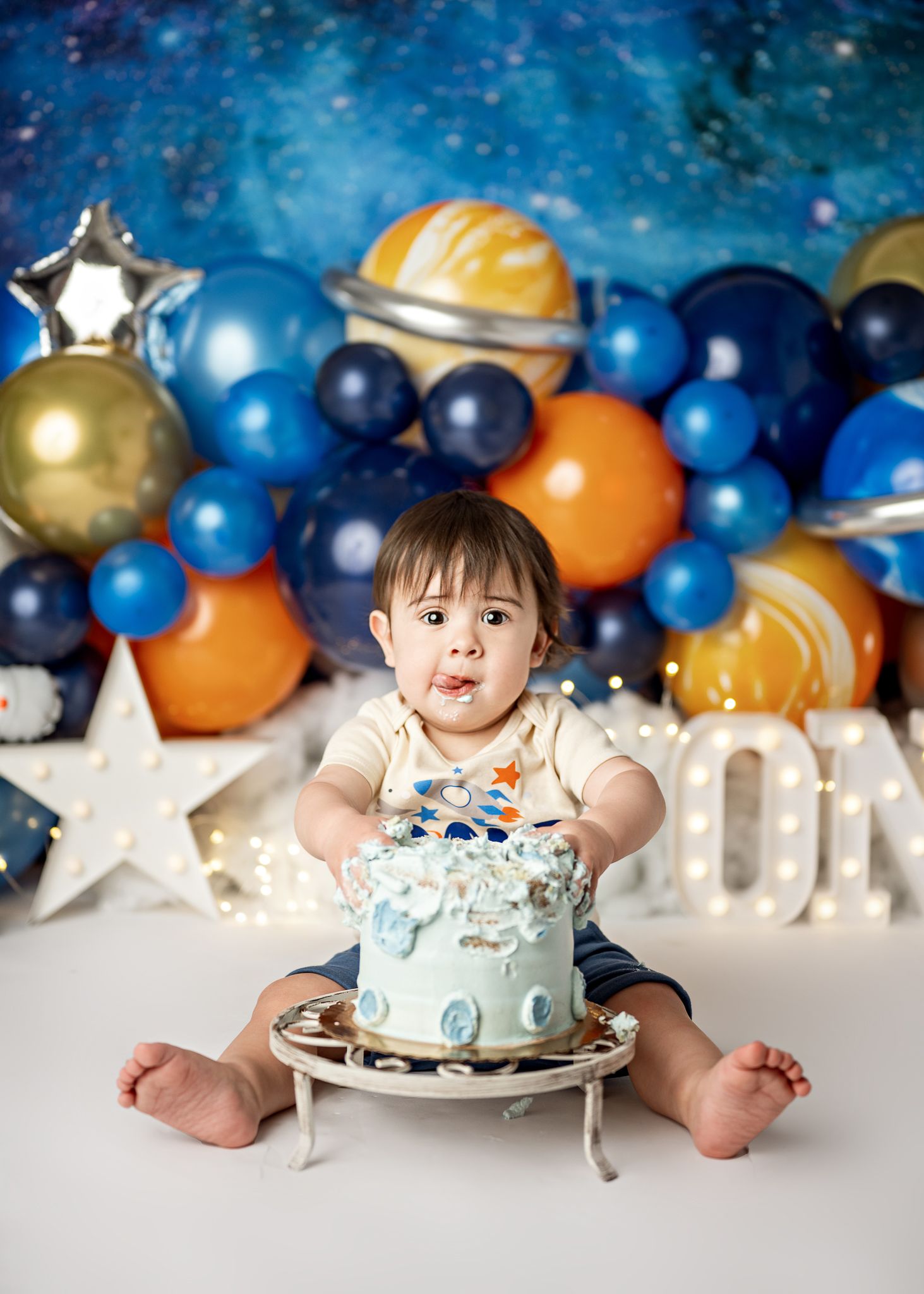 Baby sits among blue and orange balloons in a celestial-themed birthday photo shoot setup.