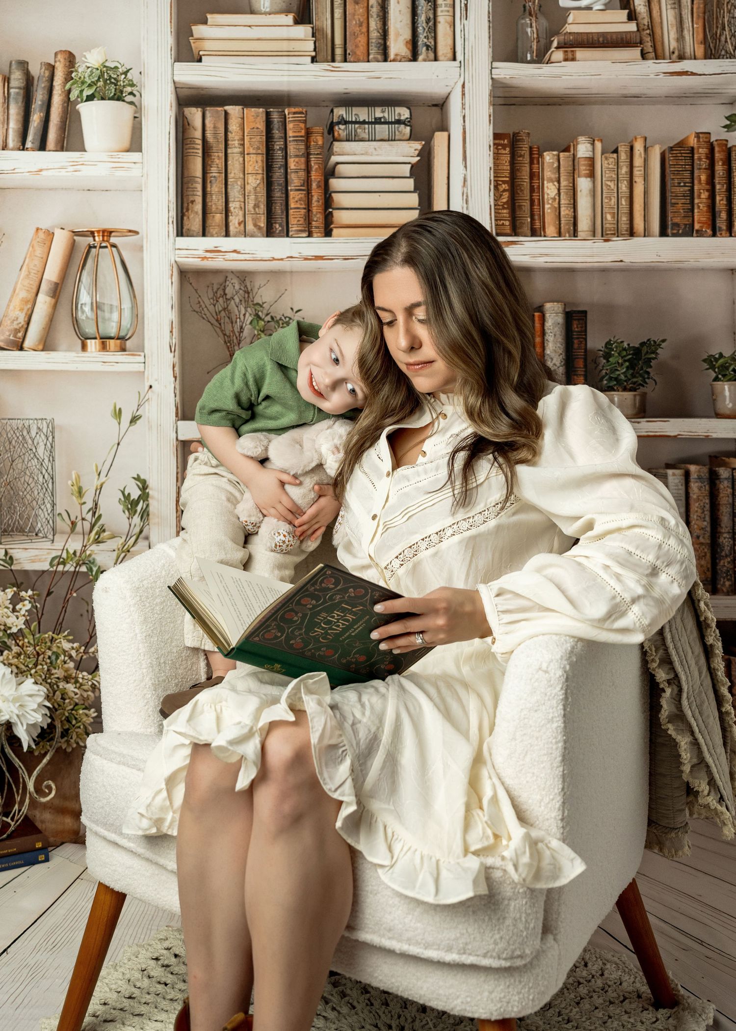 A cozy reading scene with a person and child in white attire lounging together on a chair against bookshelves.