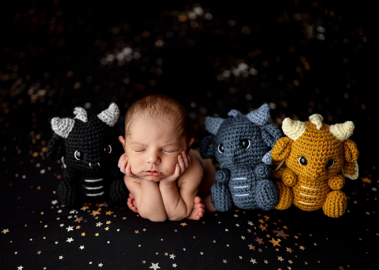 Newborn photography session featuring soft knitted elephant toys in gray and yellow against a dark backdrop.