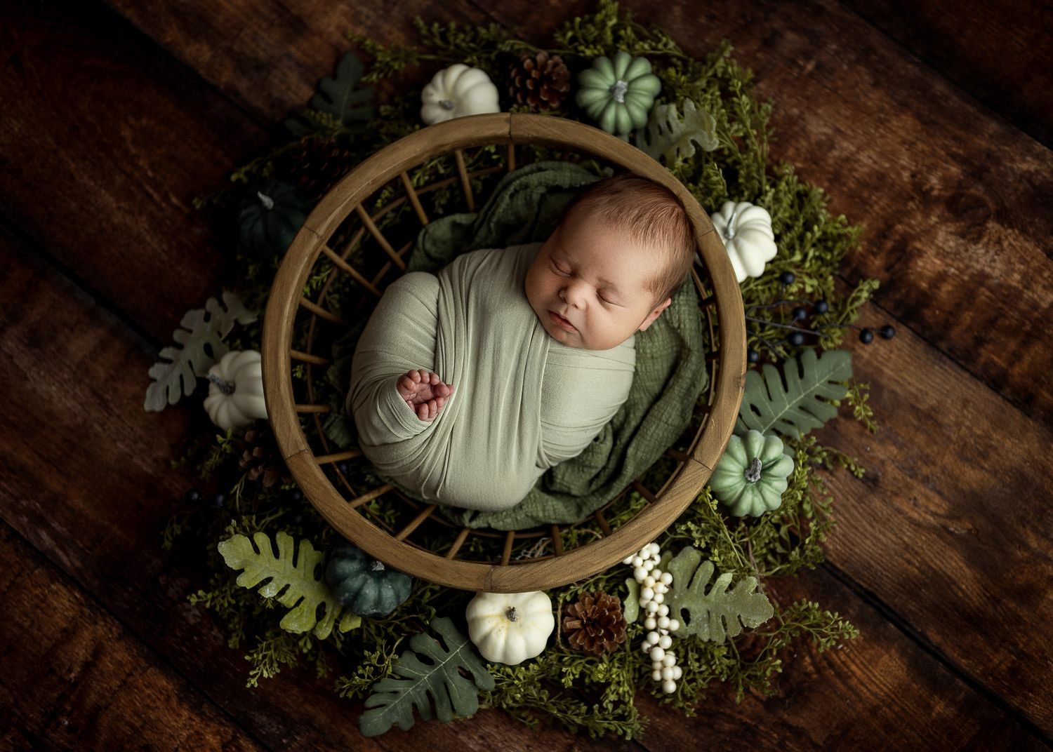 Overhead newborn photography setup with wooden basket, white bedding and delicate floral arrangements.