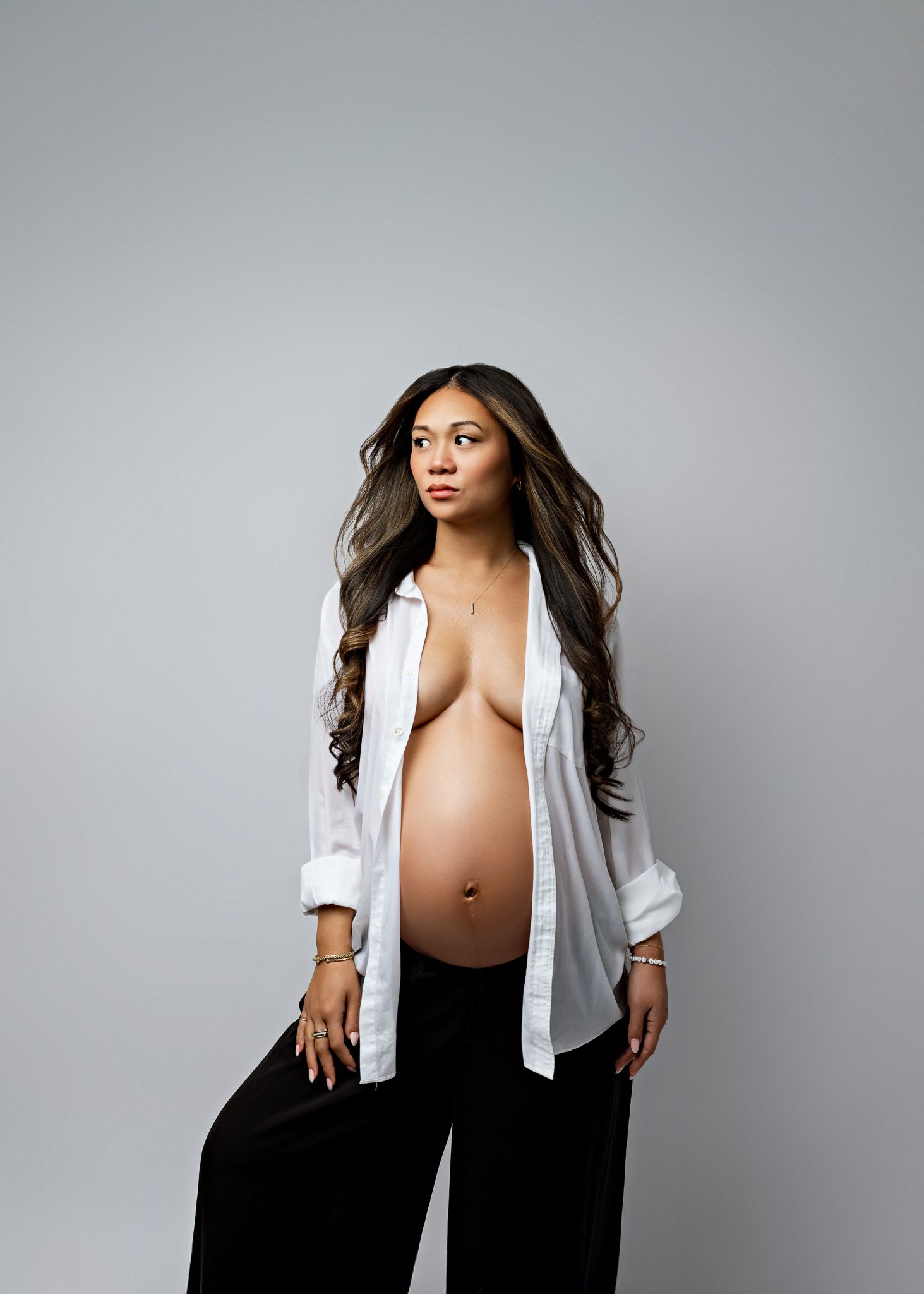 A series of four artistic maternity photos showing a woman in a white shirt and black pants against a gray backdrop.