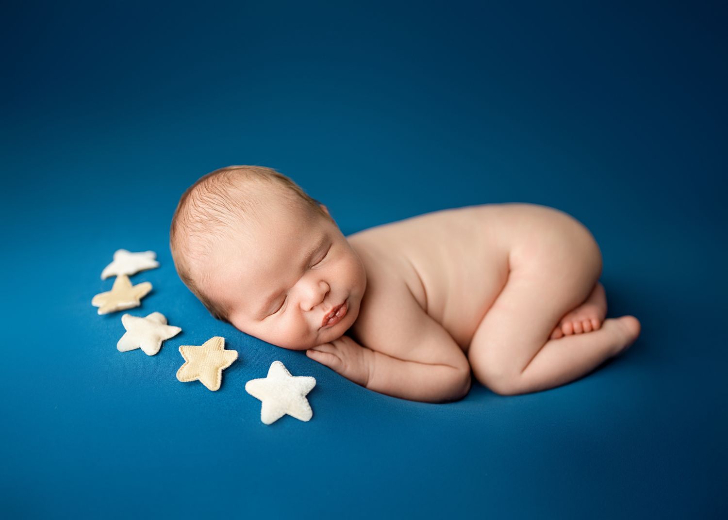 Sleeping newborn baby posed with star decorations against a deep blue backdrop.