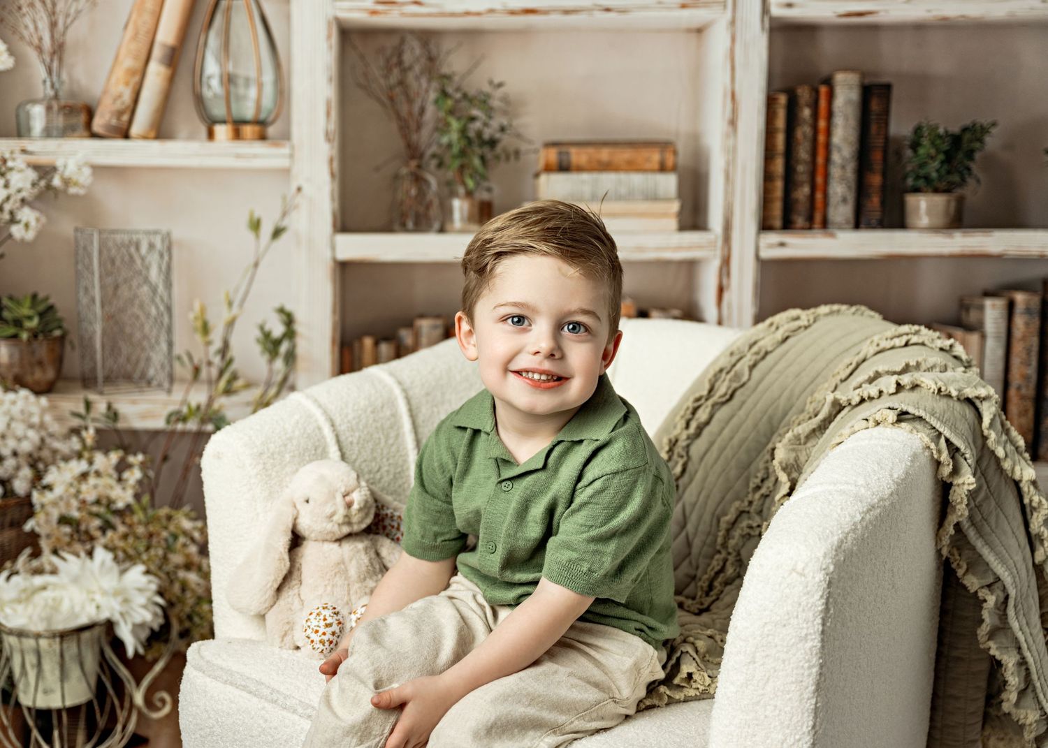 A cozy living room setting with a white armchair and decorative elements including plants and shelving in the background.