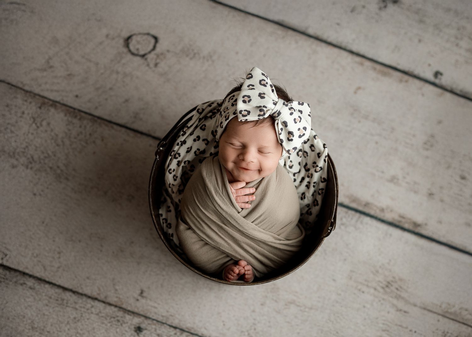 A series of artistic black and white photographs showing a newborn baby in a wooden floor setting.