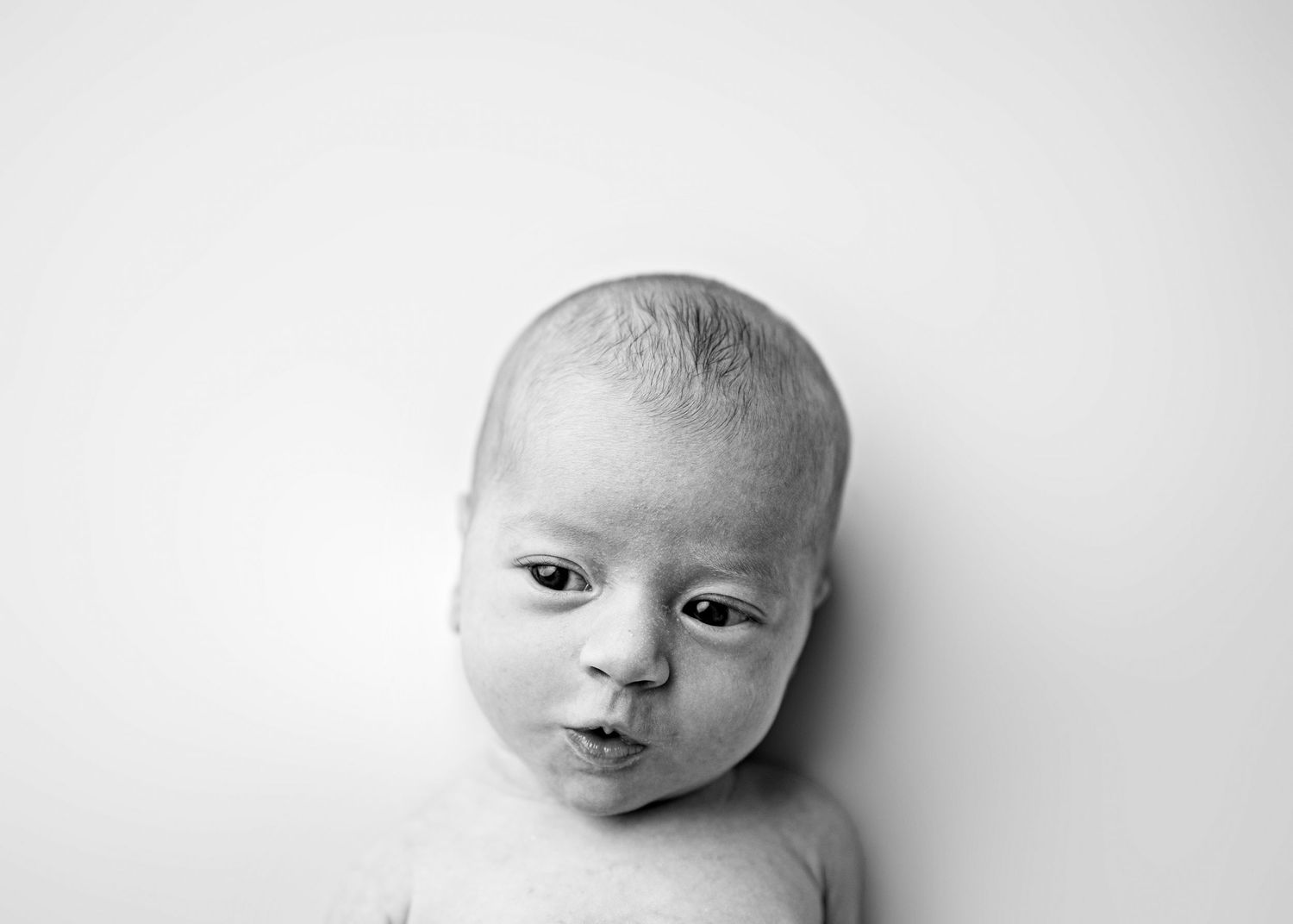 A series of black and white portraits showing a newborn baby from different angles.