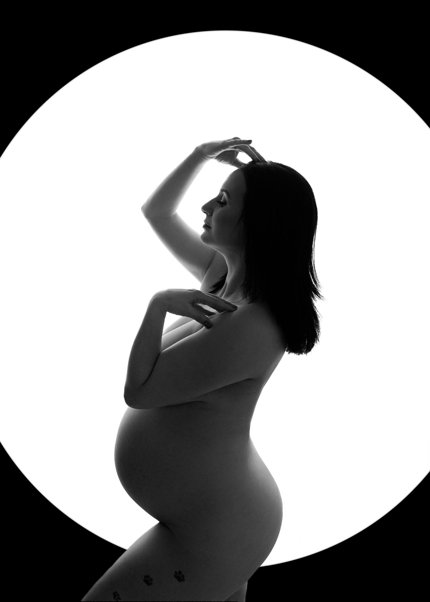 High contrast silhouette of pregnant woman in artistic pose against circular white backdrop.