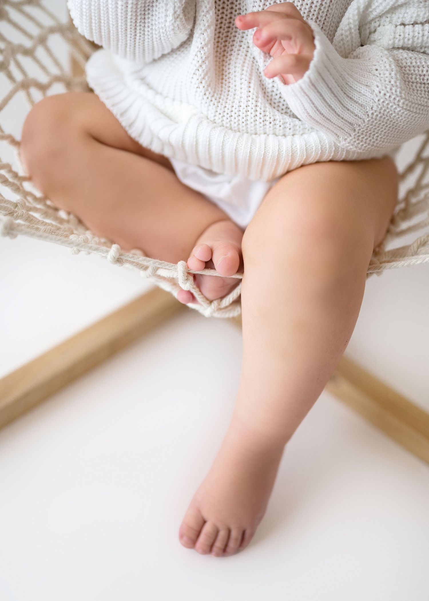 Small bare foot and leg of someone wearing a white knit sweater while sitting on a cream-colored surface.