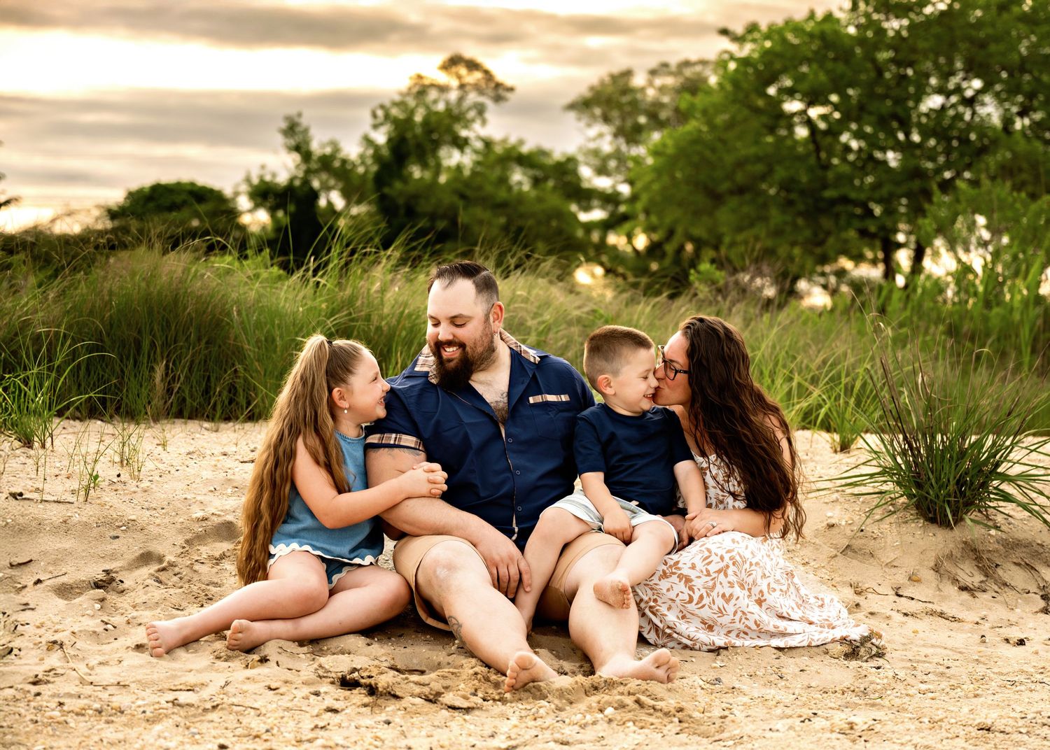 Family lying on sandy beach during golden sunset in casual attire for outdoor photo session.