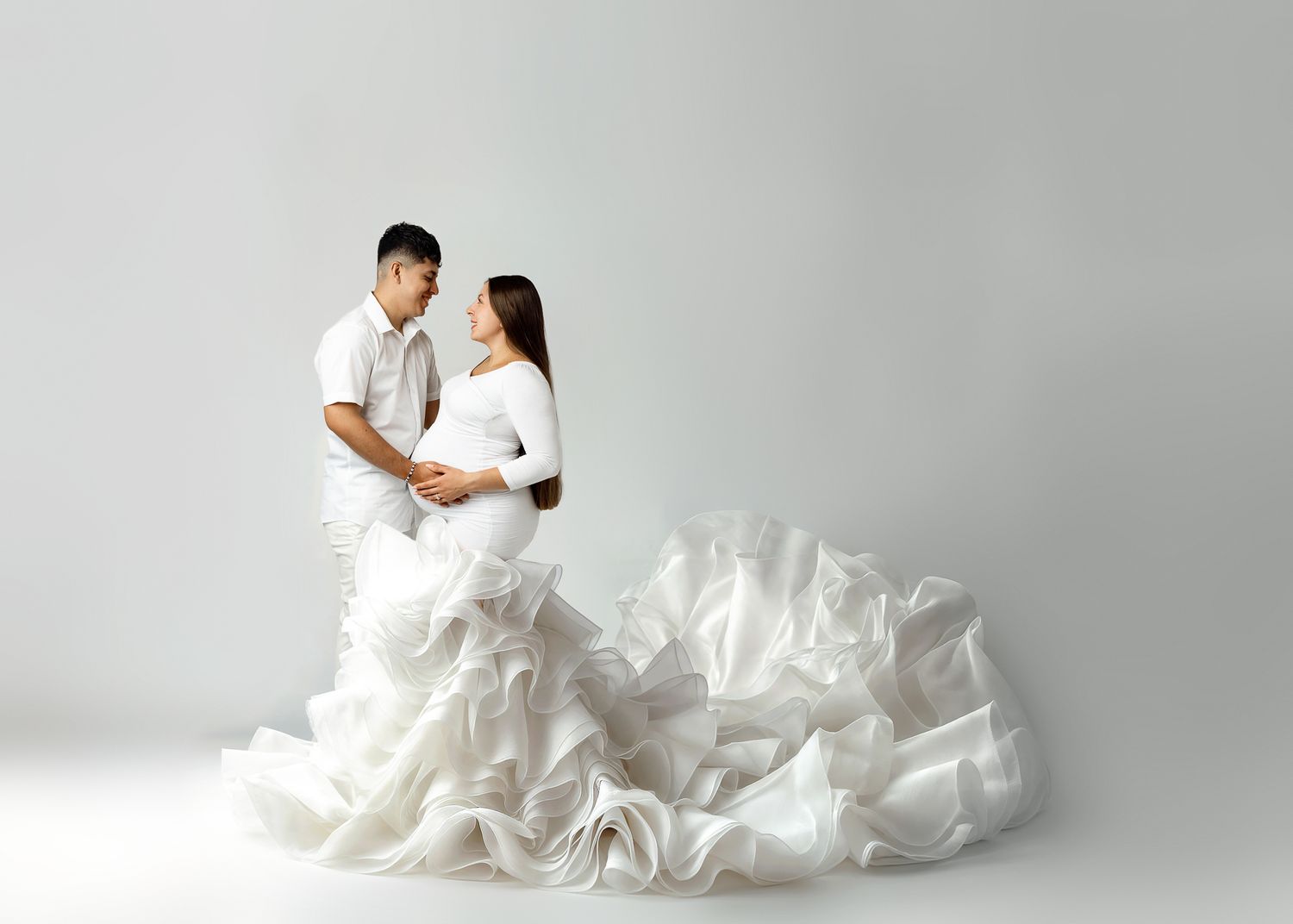Minimalist couple's portrait with flowing white fabric creating dramatic movement against gray background.