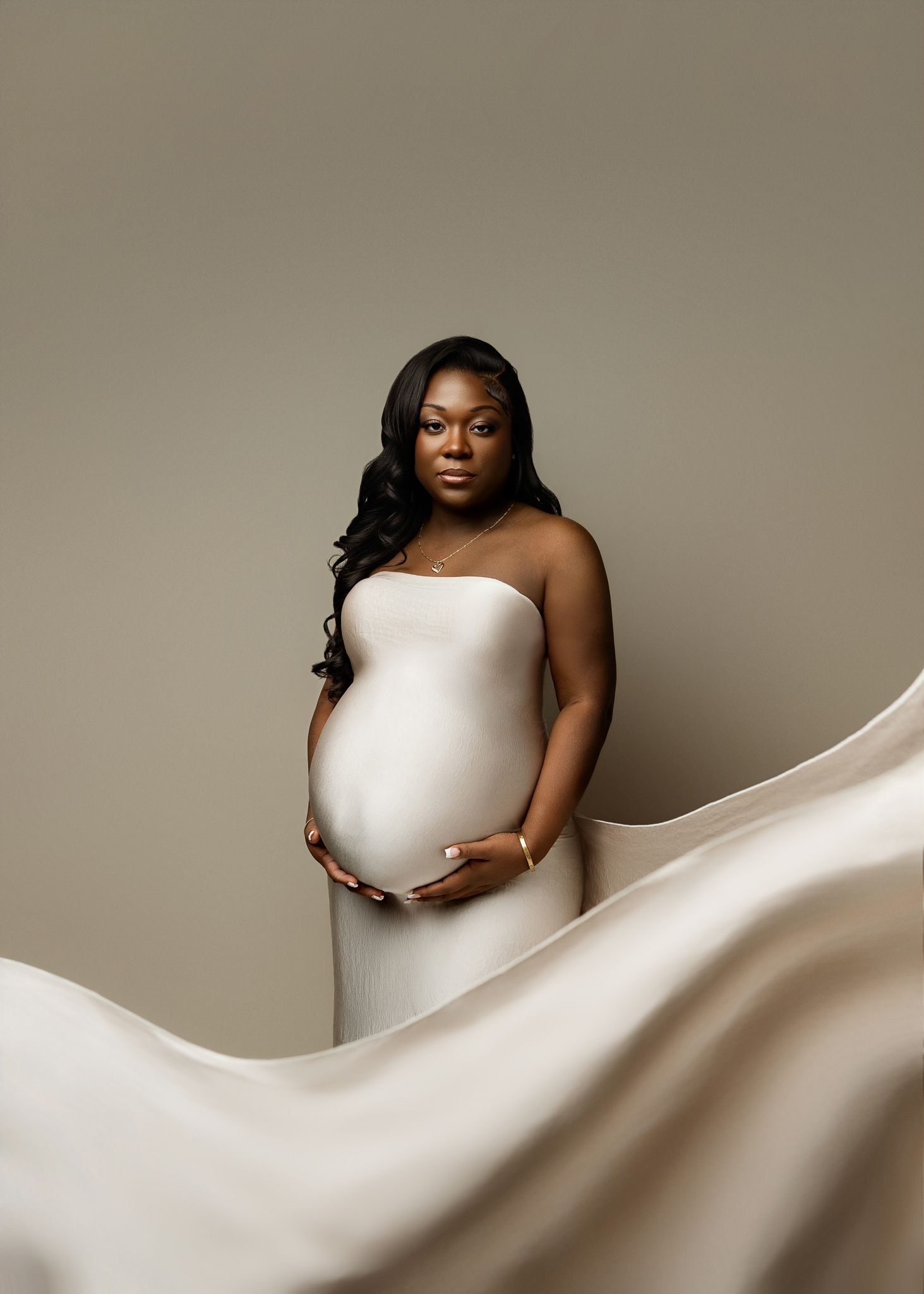 Elegant maternity portrait series with flowing white fabric against neutral backdrop showcasing pregnancy journey.