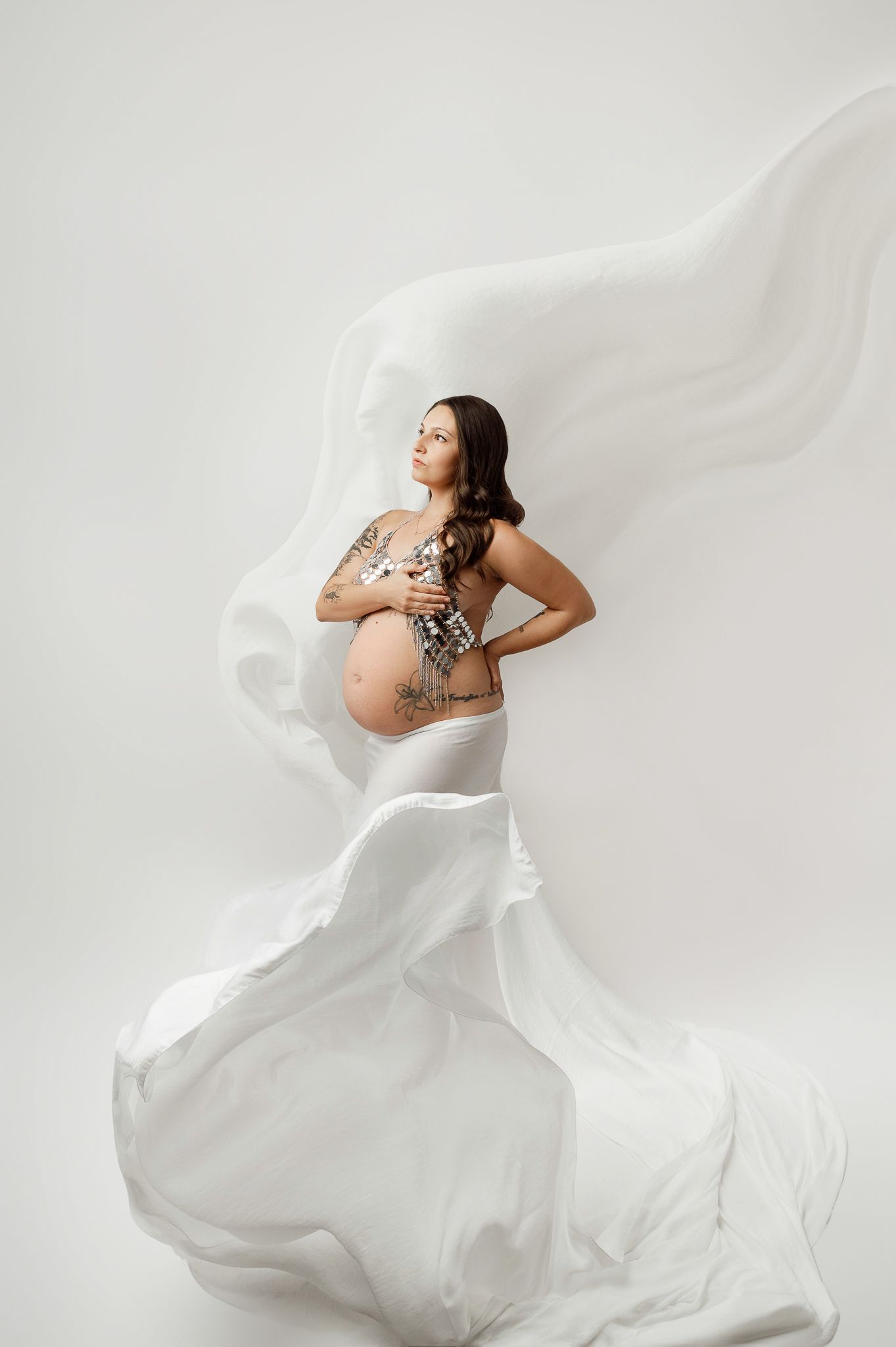Artistic maternity portrait with flowing white fabric creating ethereal movement against neutral background on Long Island, NY