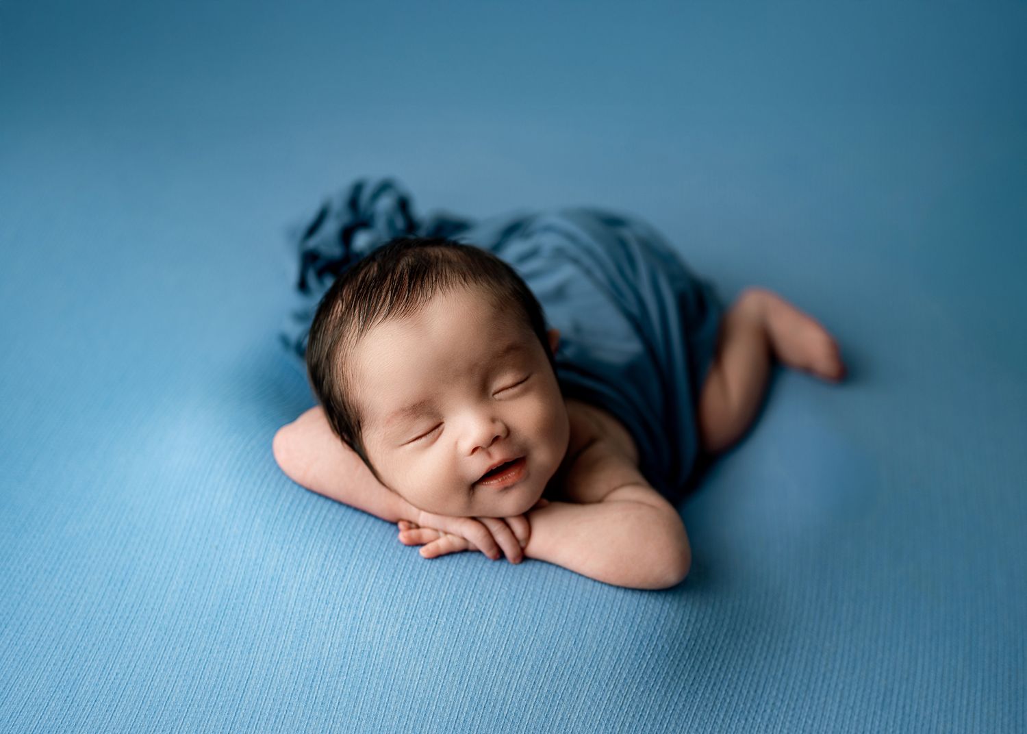 Sleeping newborn wrapped in blue fabric lying on blue blanket during professional photo session.