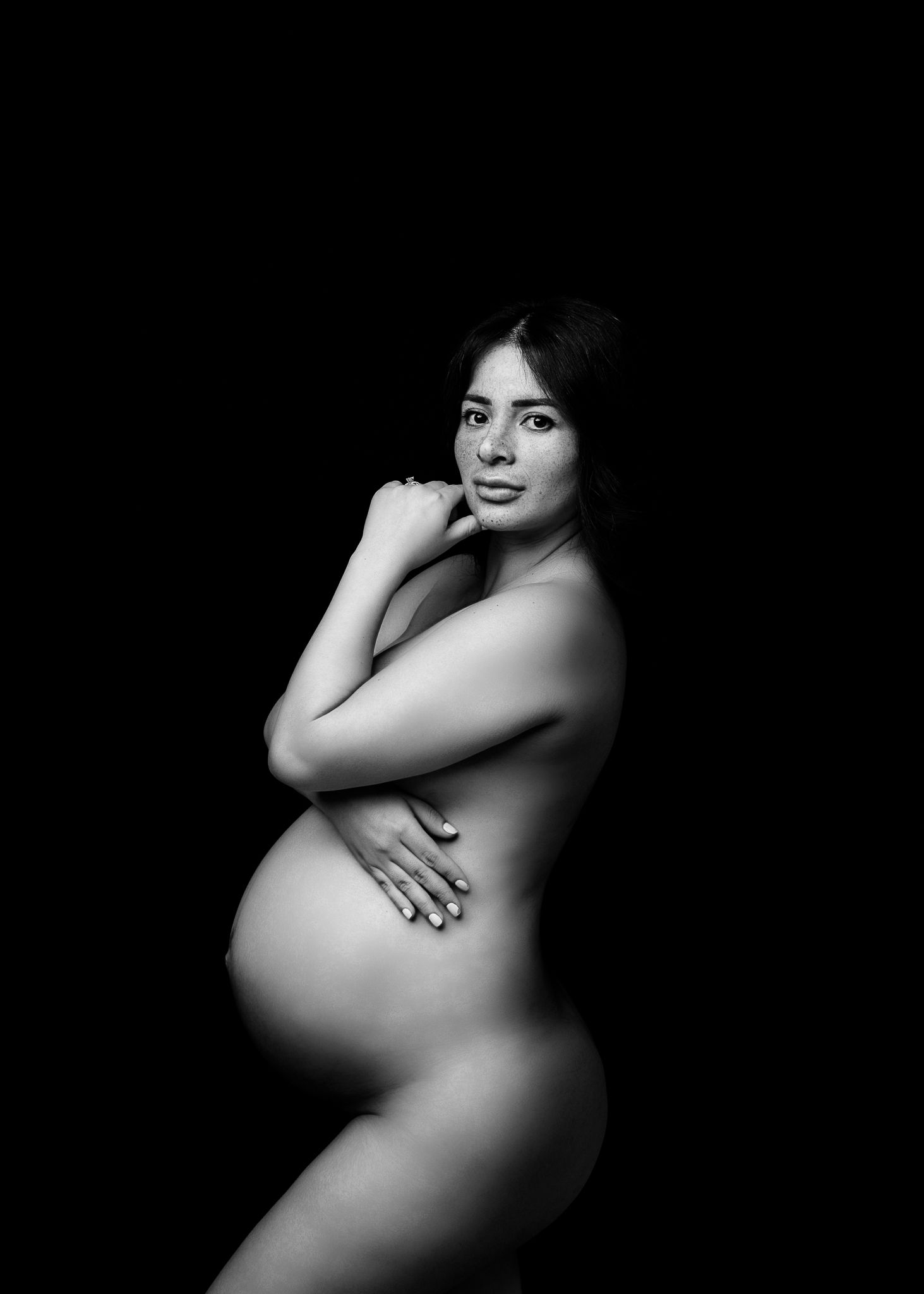 Artistic black and white maternity photo showing silhouette of pregnant woman against dark background.