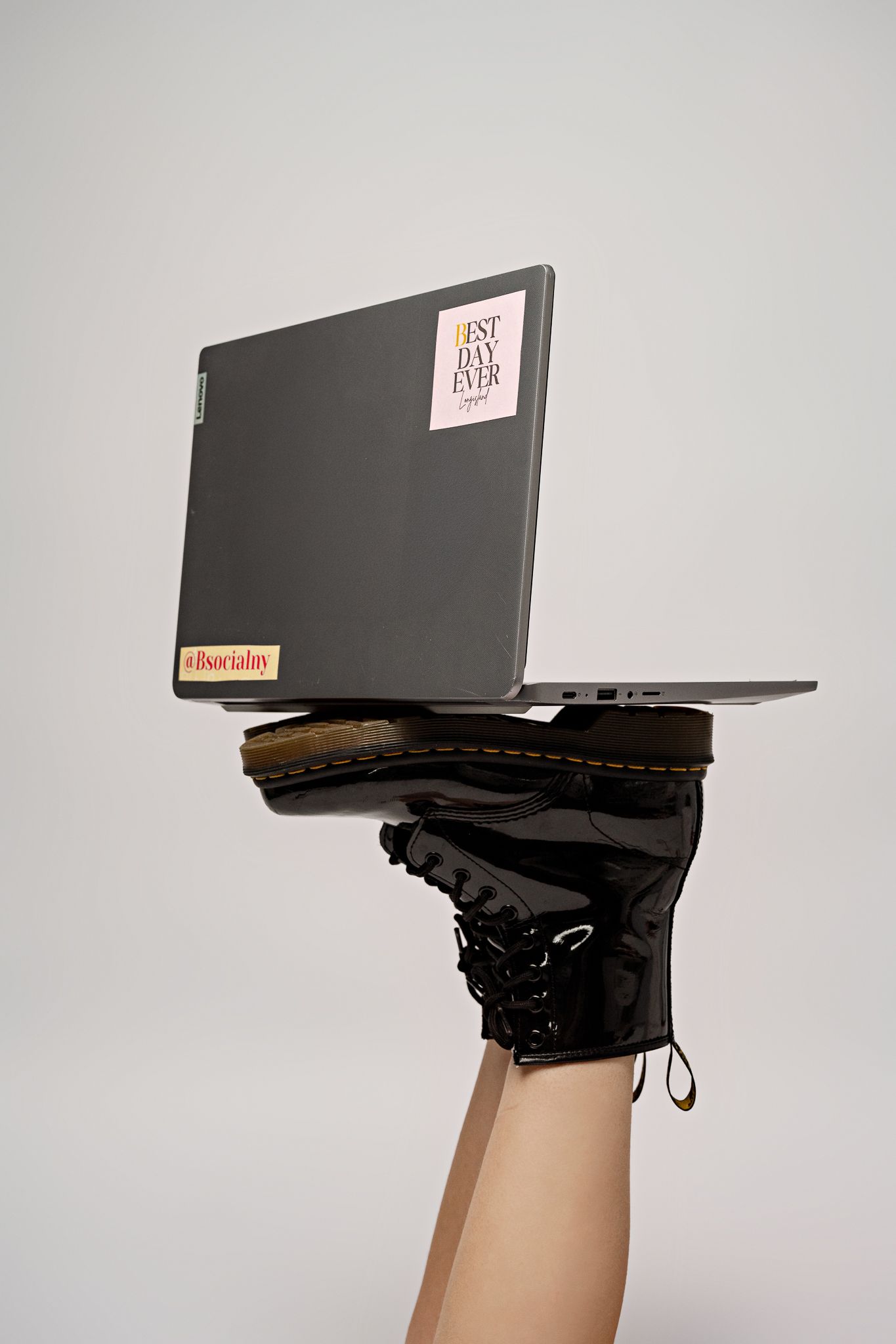 Black laptop balanced on combat boot against light gray background in creative product photography.