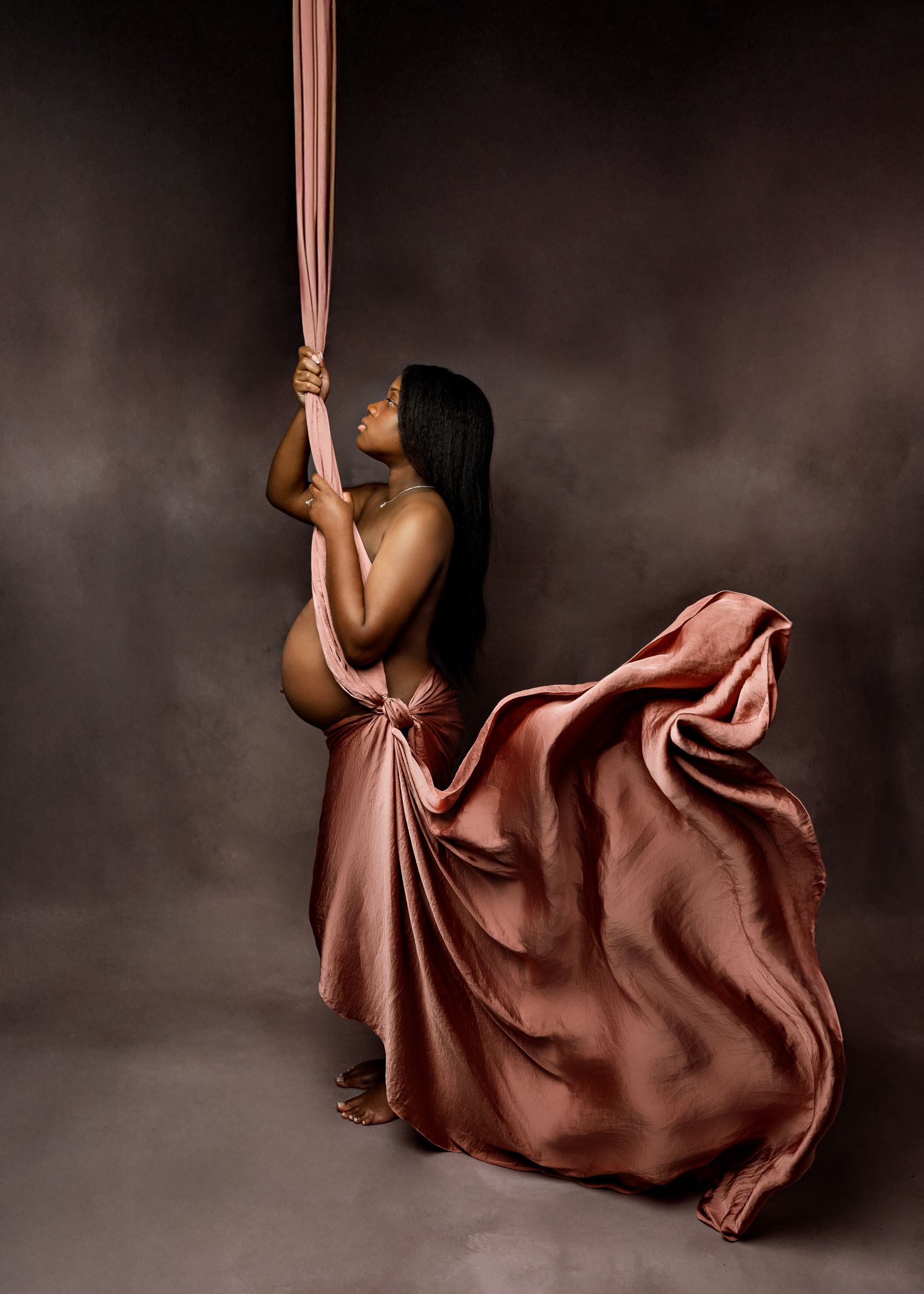 A series of aerial dance photos showing a performer in a flowing brown dress suspended from silk ribbons against a dark background.