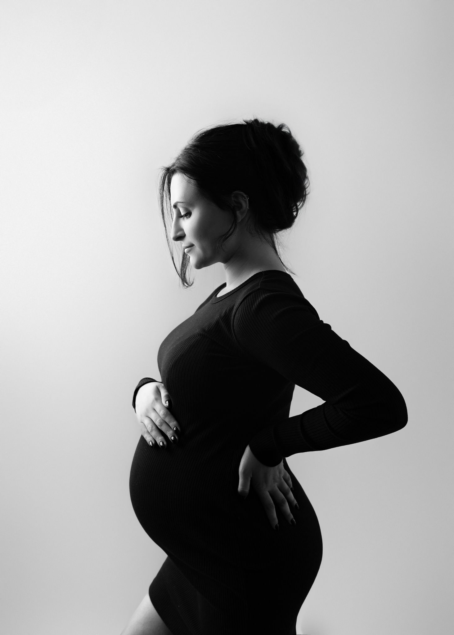 Black and white profile portrait of pregnant woman in dark clothing against light background.