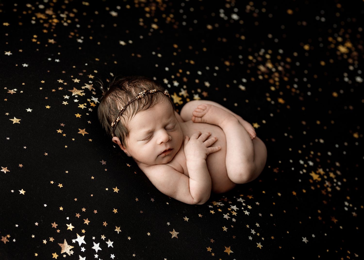 Gold glitter confetti sparkles scattered on black background in artistic newborn photo session series.