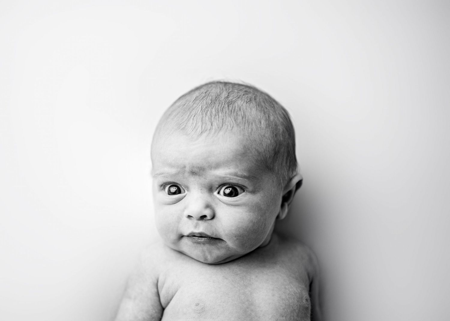 A series of three black and white close-up portraits of a baby showing different facial expressions.
