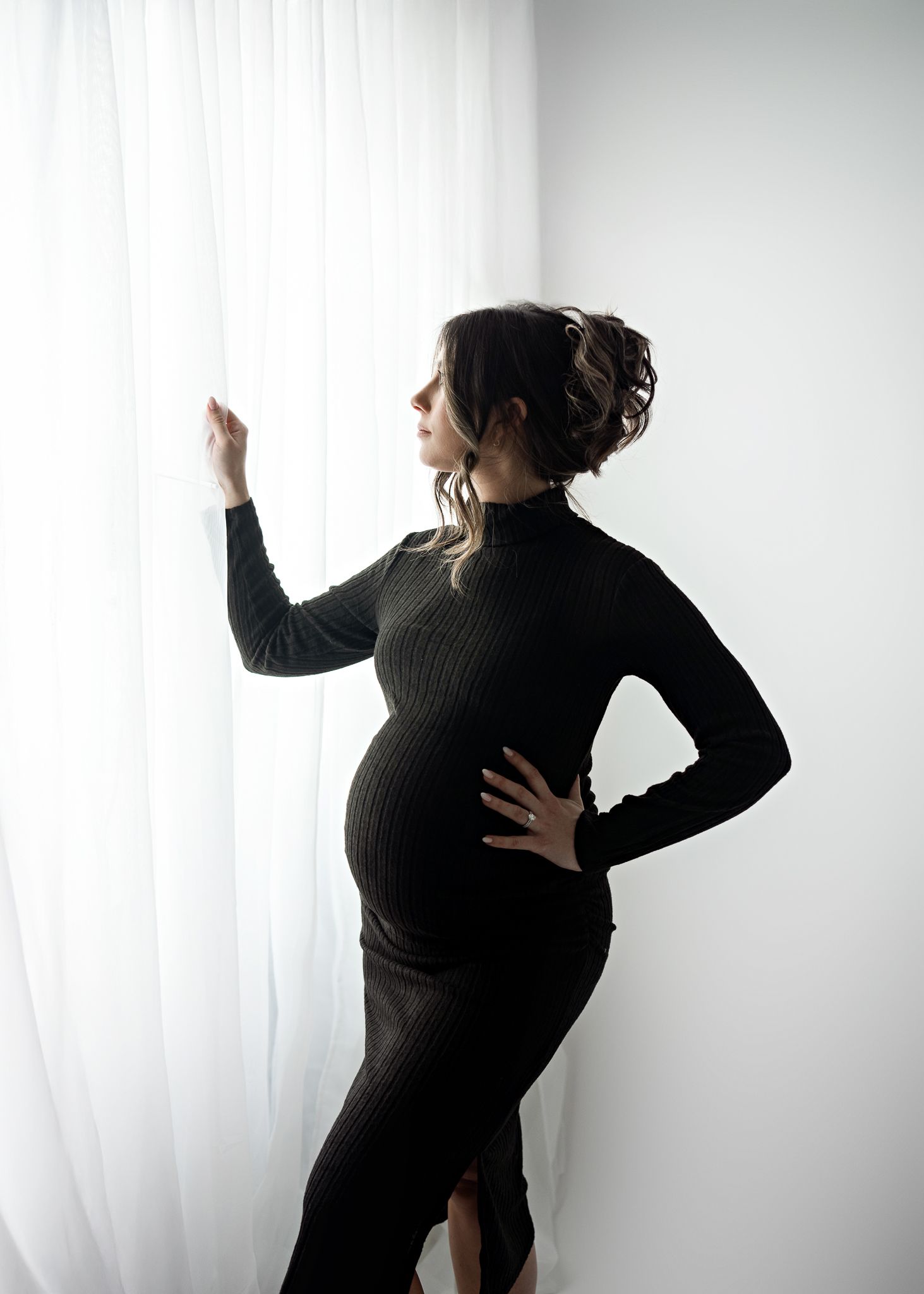 Elegant maternity silhouette by window showing pregnant figure in black sweater dress.