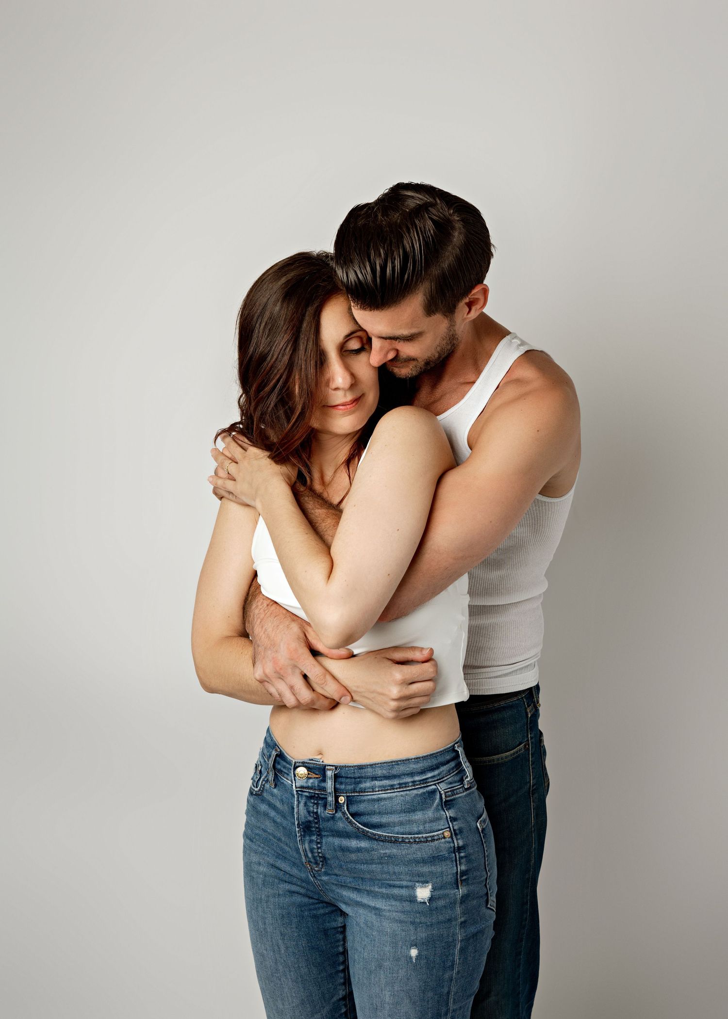 Two people embrace intimately in white and denim against neutral backdrop showing progression of romantic poses.