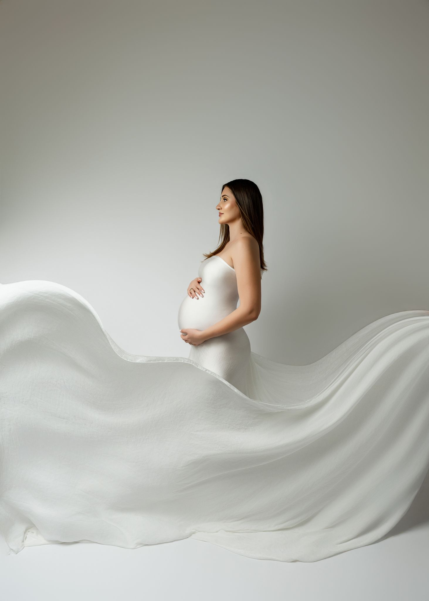 A minimalist maternity photo series shows a white fabric flowing elegantly across four progressive pregnancy stages.