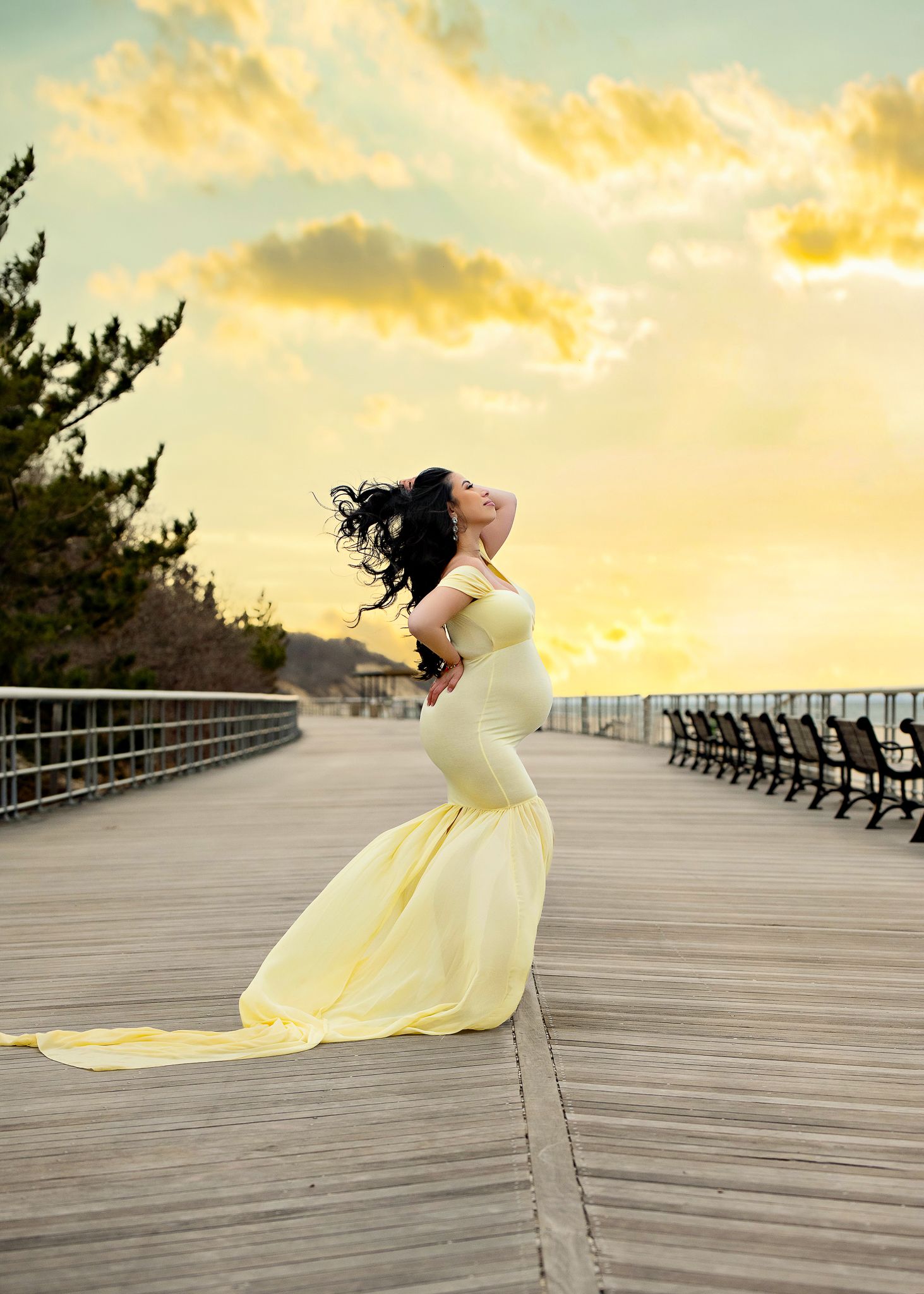 Figure in flowing yellow dress poses dramatically on boardwalk during golden sunset.
