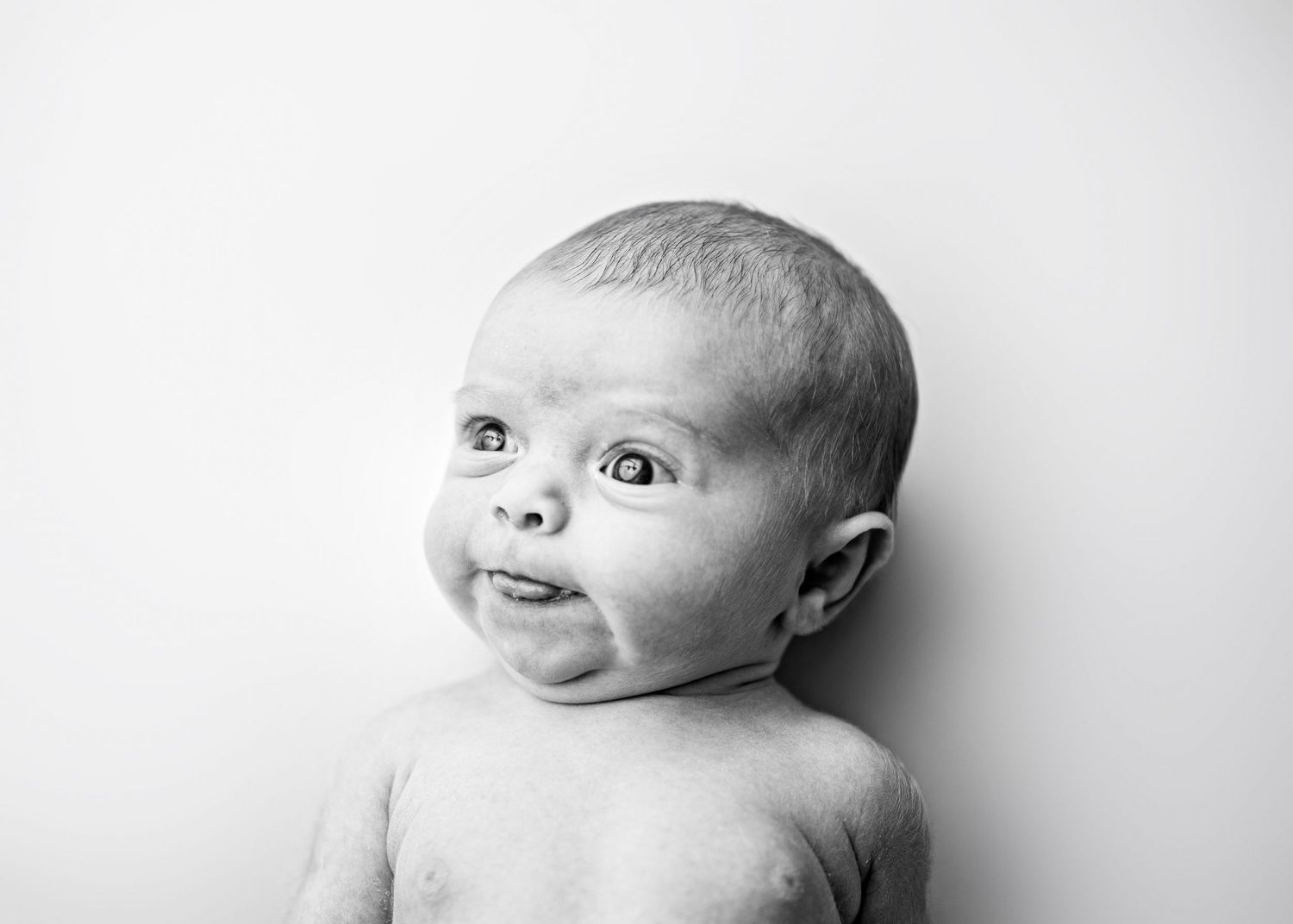 Black and white portrait of a baby with wide eyes and expressive face against a light background.