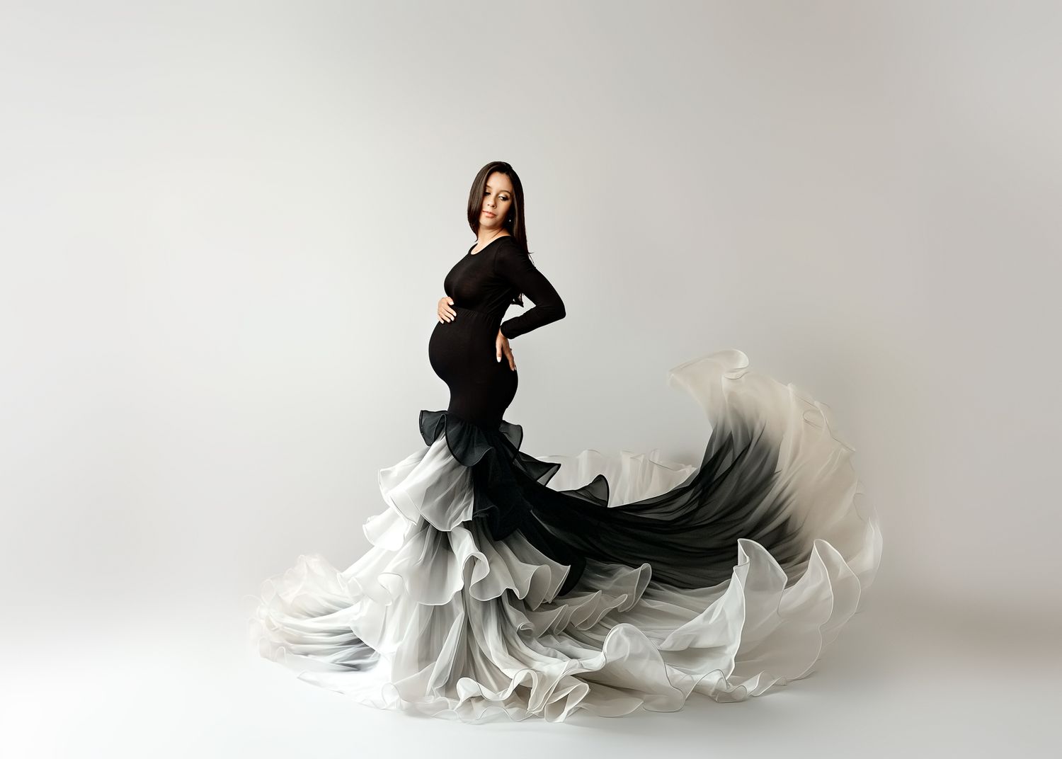 Elegant figure in flowing black and white ombre gown with dramatic ruffles poses gracefully against white backdrop in Nesconset Studio, NY