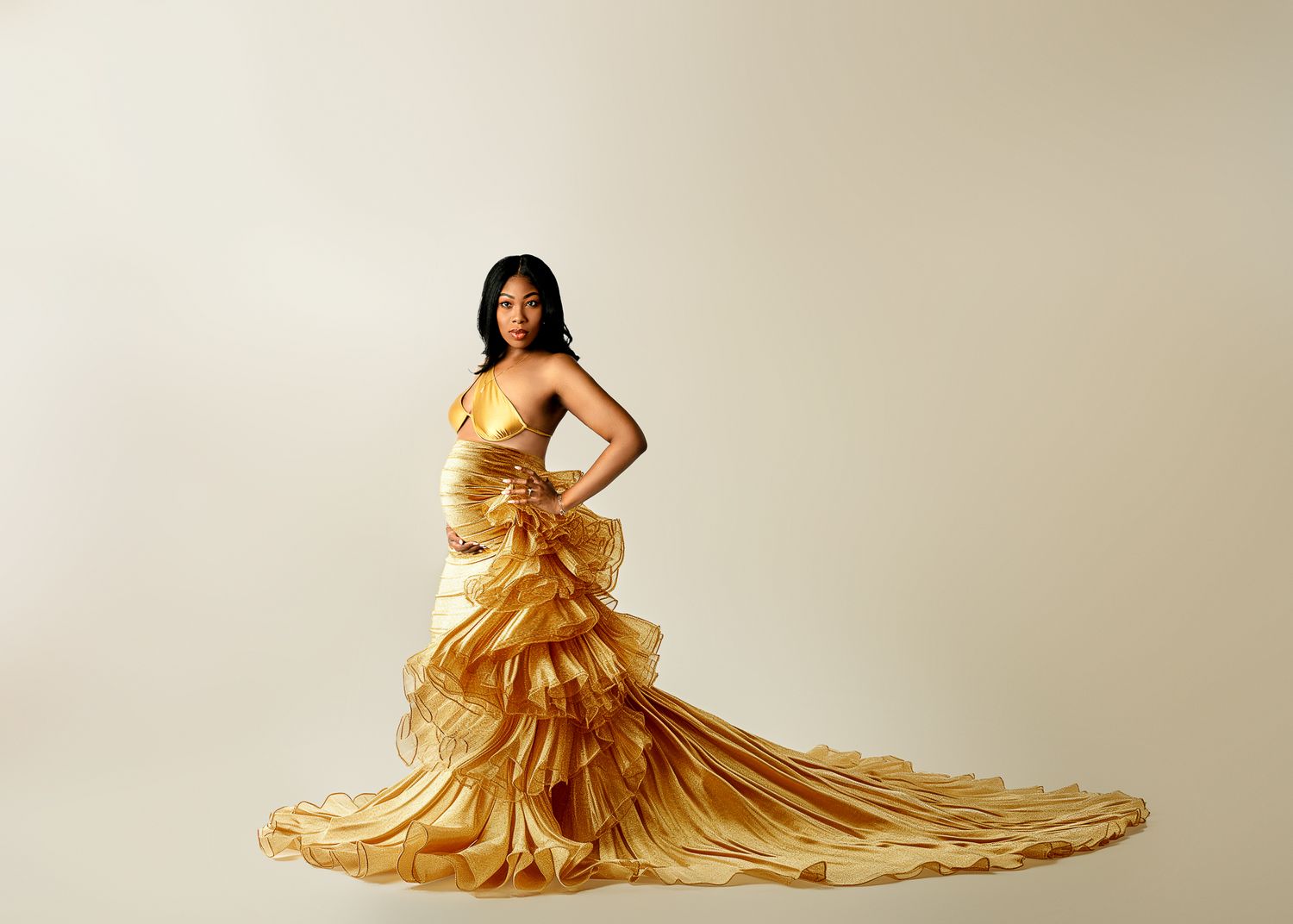 A figure poses in a dramatic gold ruffled gown with a flowing train against a neutral backdrop.
