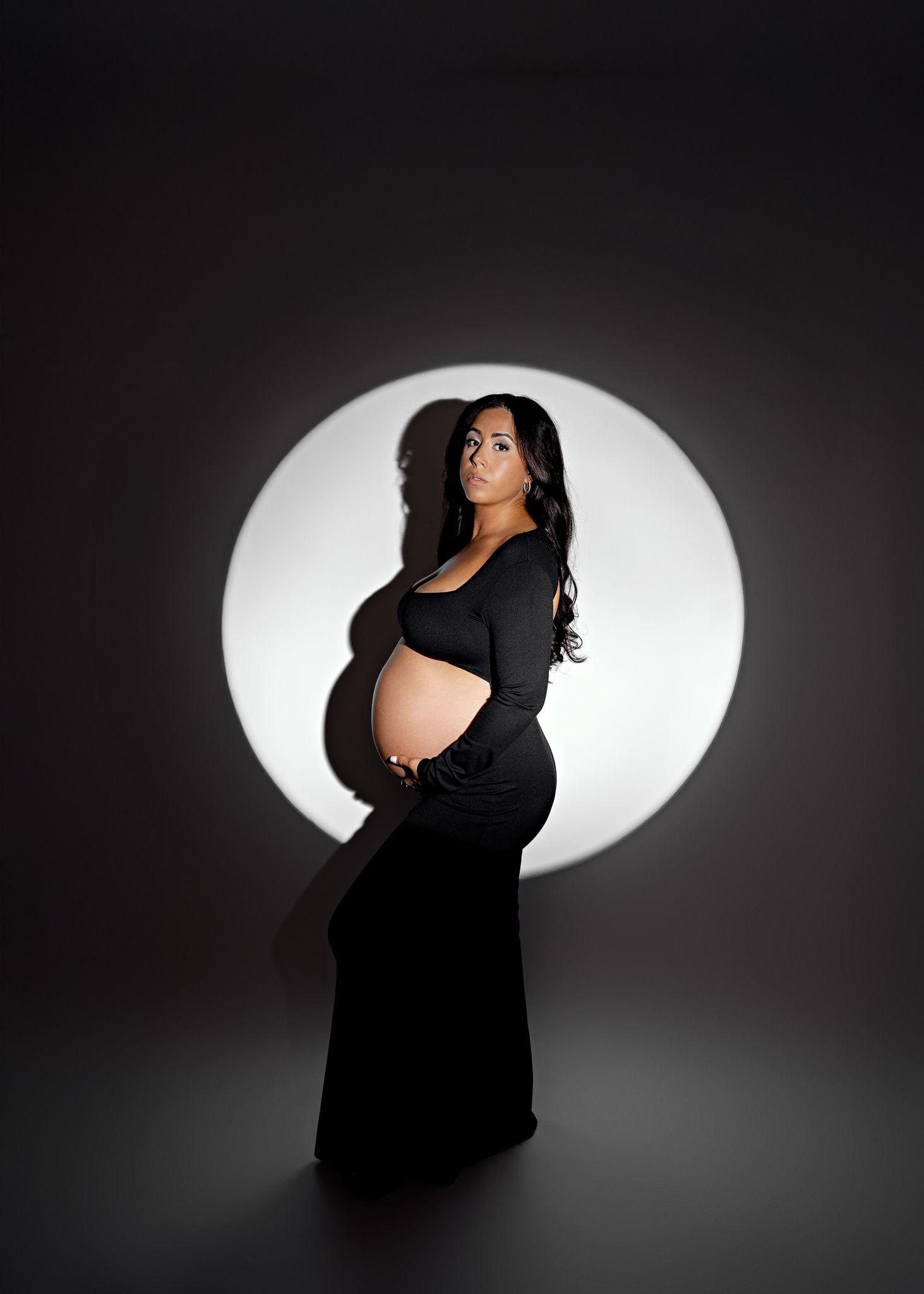 A series of silhouetted maternity portraits against a white oval backdrop showing a pregnant figure in a black dress.