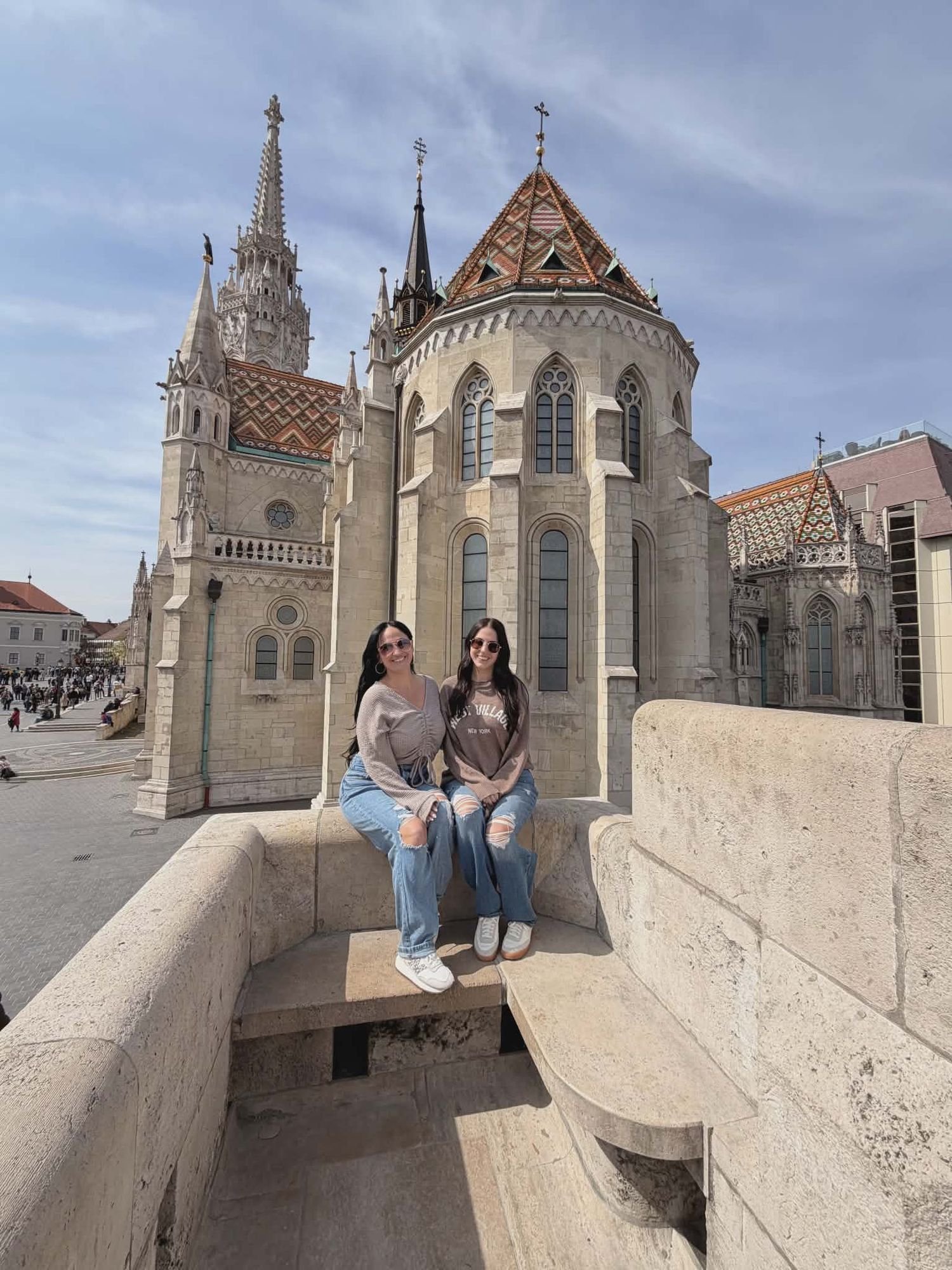 Two women sitting on stone steps in front of Matthias Church at Fisherman's Bastion, Budapest, Hungary.