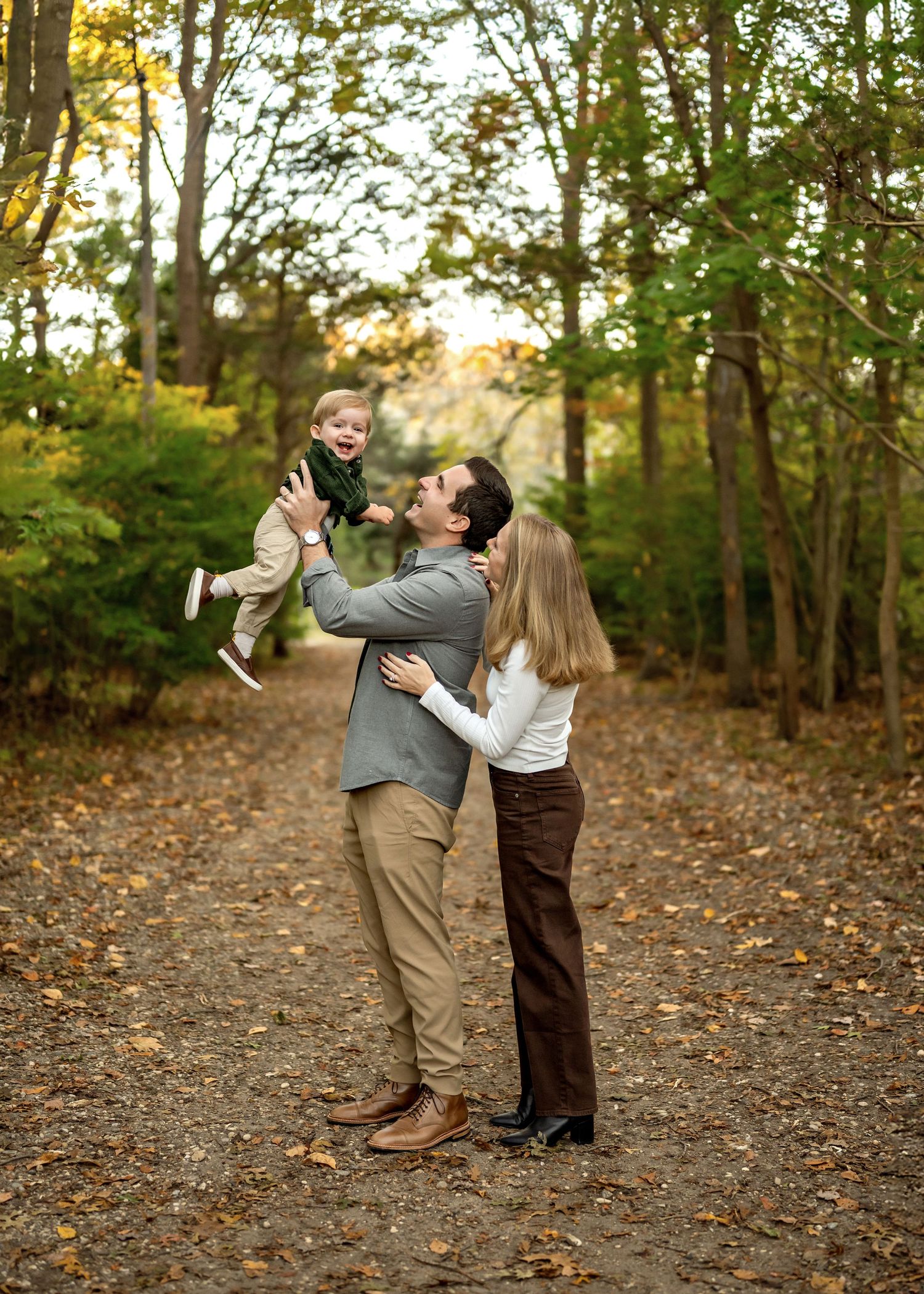 A couple embraces and dances together on a leaf-covered path in an autumn forest setting during golden hour.