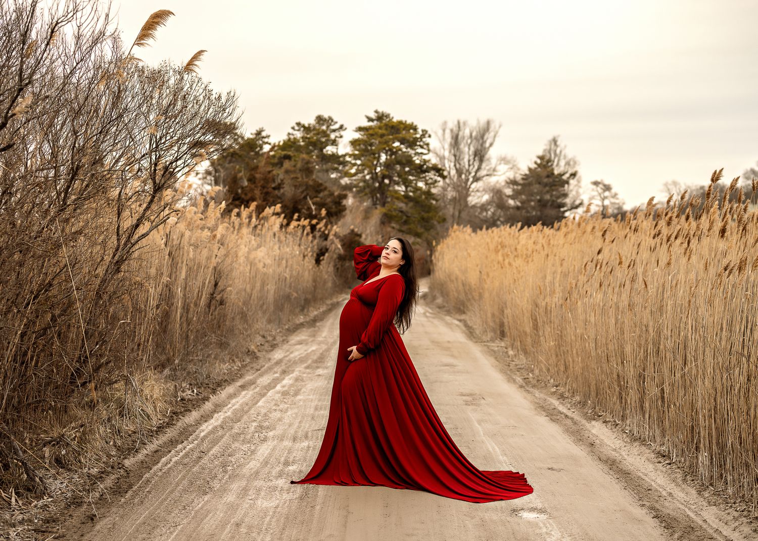 A dramatic red flowing dress stands out against golden reeds and a winding dirt path at sunset.
