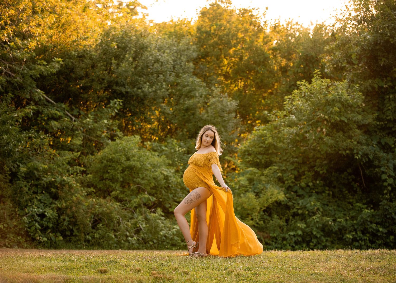Person in flowing mustard dress twirling in grassy field at golden hour with autumn trees behind.