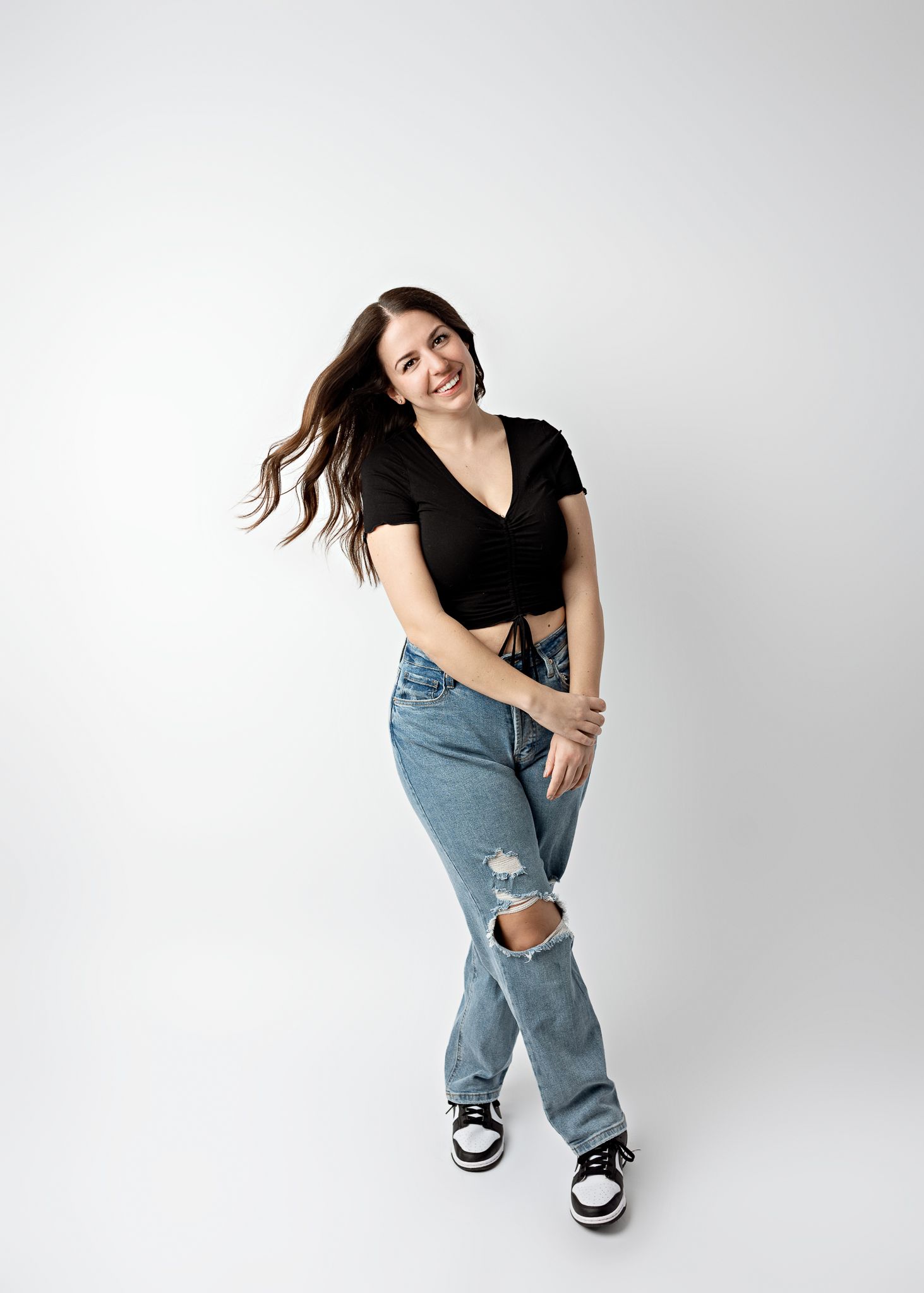 Casual portrait series with energetic poses in ripped jeans and black top against white backdrop.
