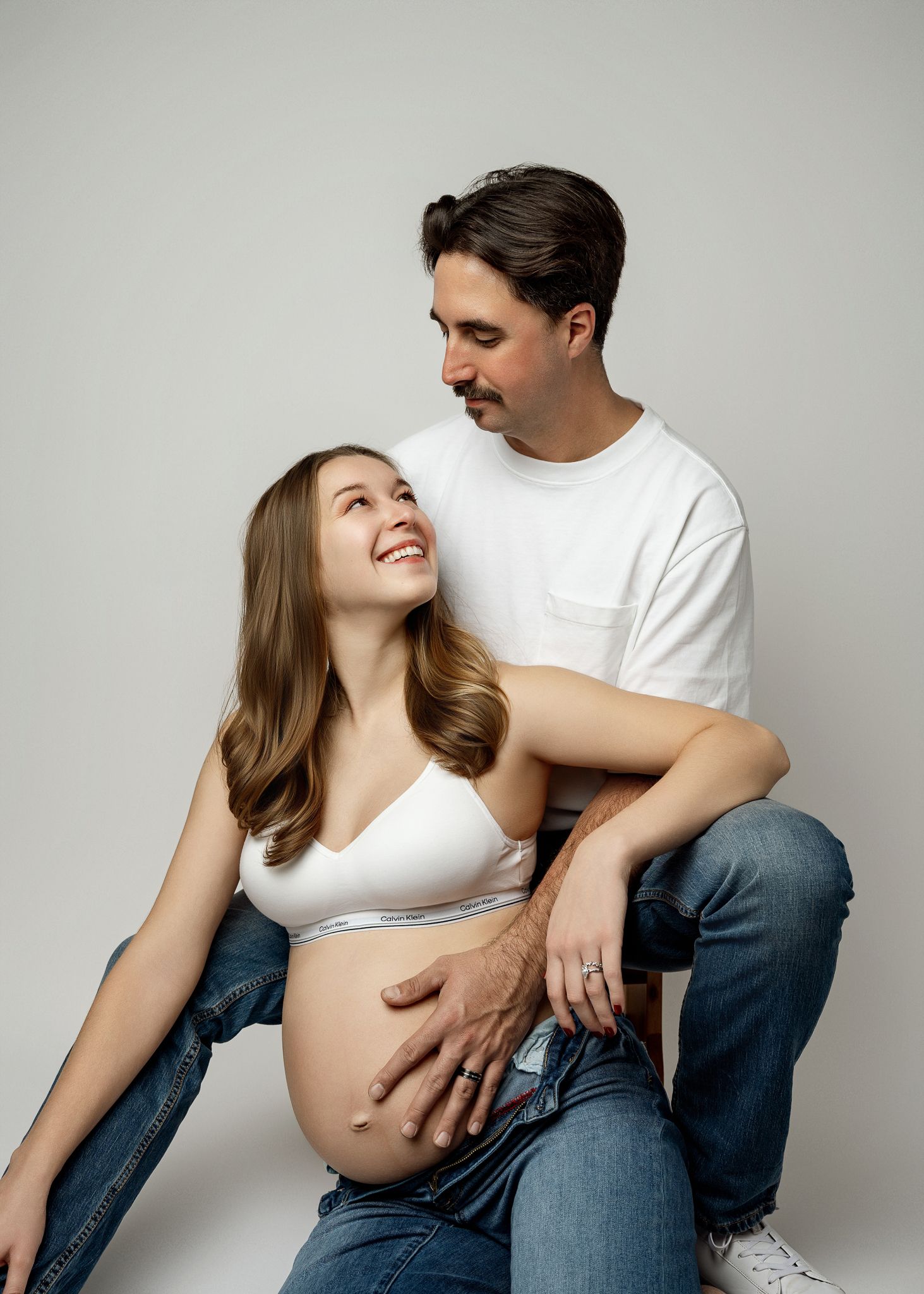 A series of intimate maternity photos showing a couple embracing against a light gray backdrop.