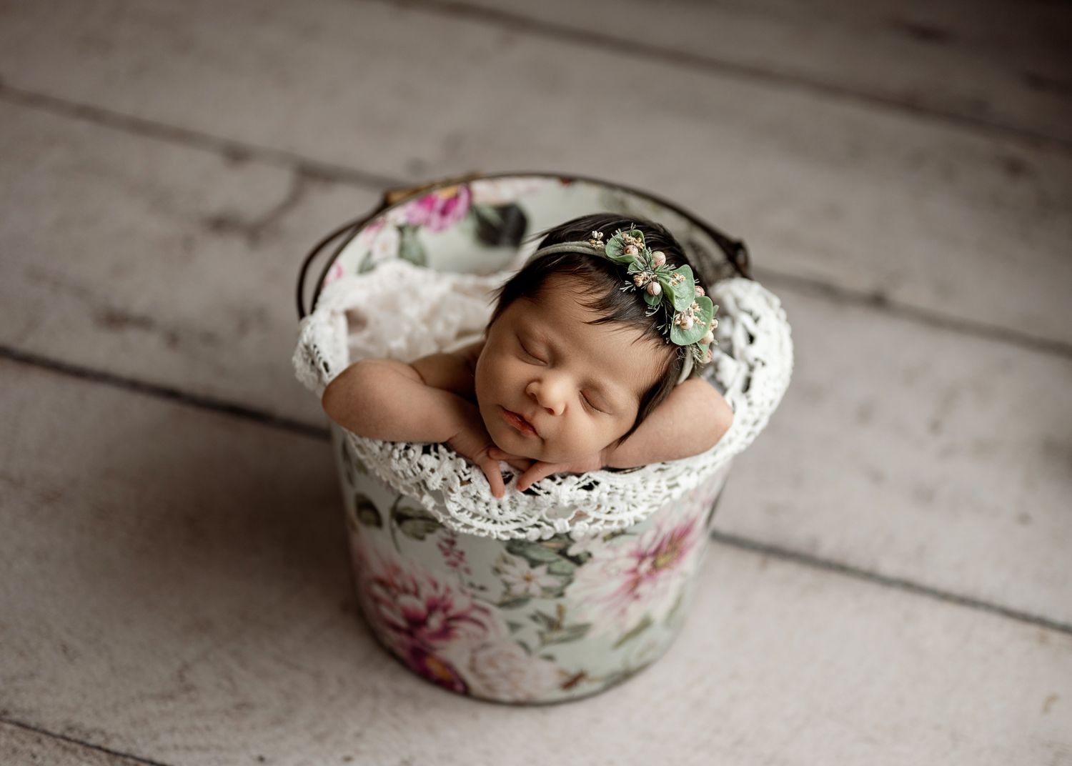 Sleeping newborn in vintage floral bowl against rustic white wooden floor background.
