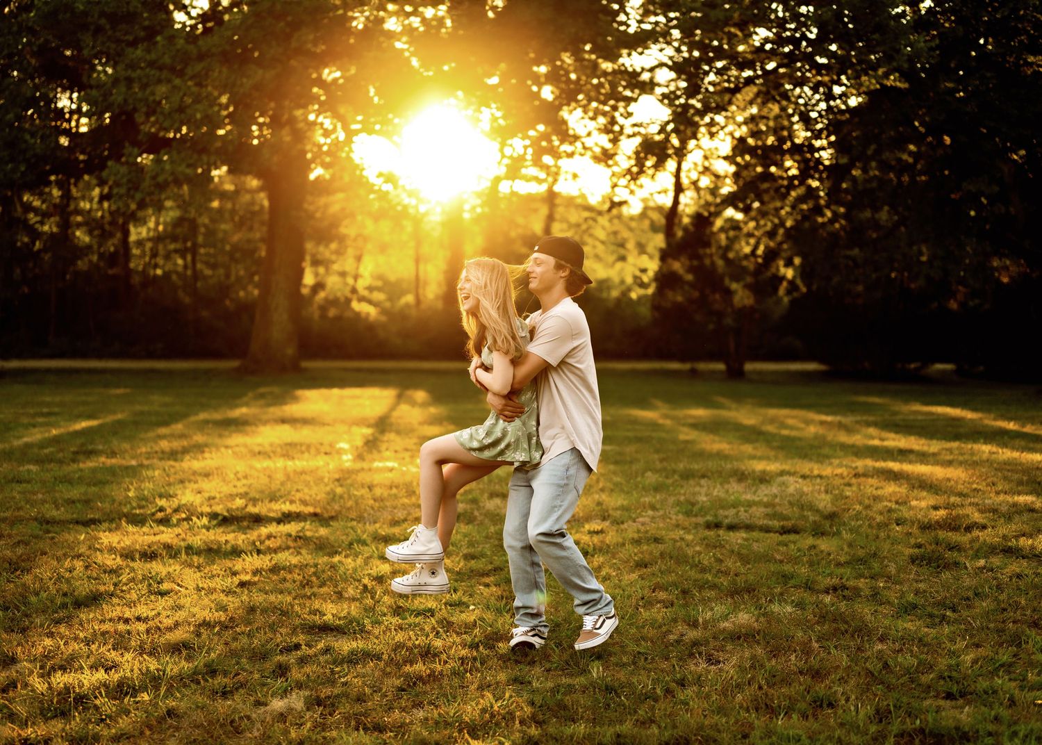 Two people dancing together in a grassy field at sunset with golden sunlight streaming through trees.