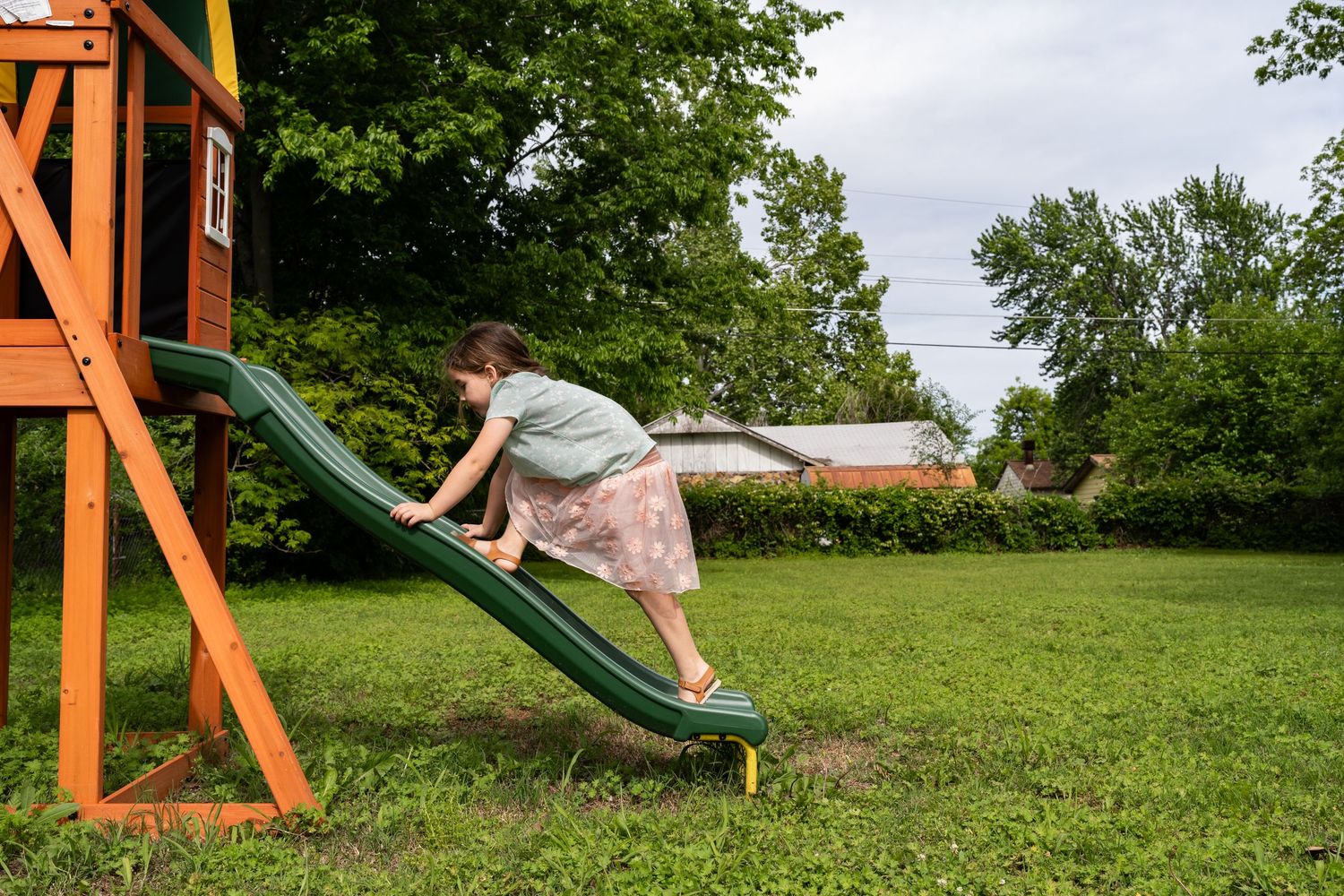 Photographer photographs girl climbing up a slide during a backyard family documentary session in Tulsa, Oklahoma