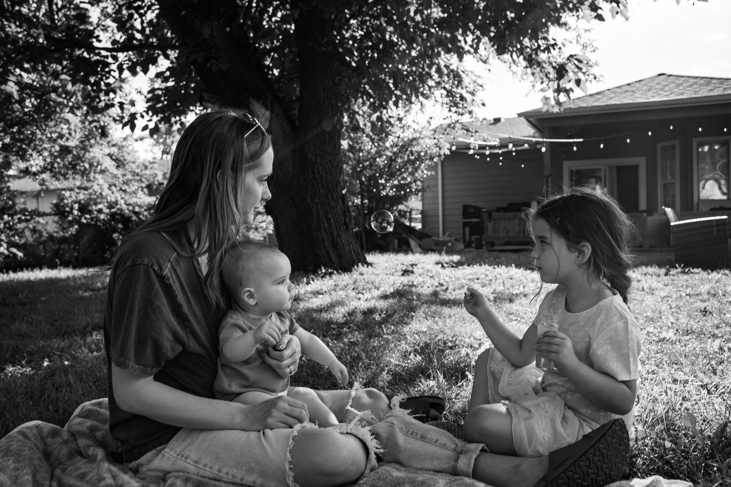 Mom and kids blow bubbles together in backyard family documentary photography session in Tulsa, Oklahoma