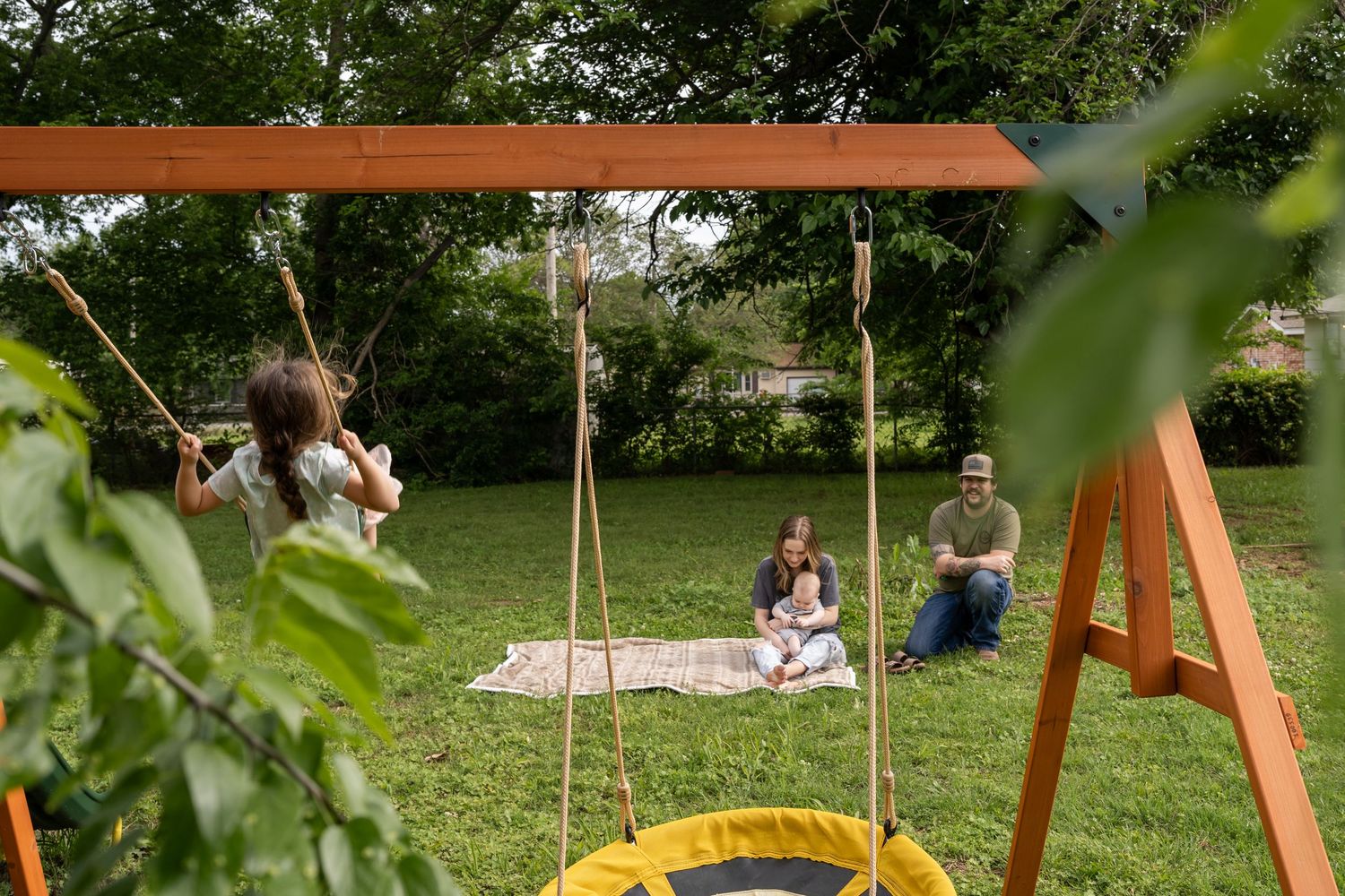 Candid Tulsa family, in backyard family photography session: Mom, dad, and baby on blanket, watching daughter swing on swingset