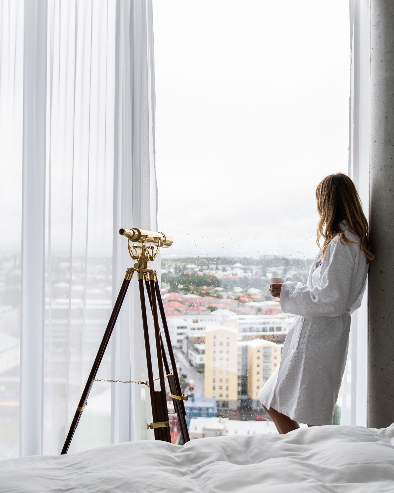 Several telescopes on tripods are set up near large windows overlooking a cityscape on a bright day.