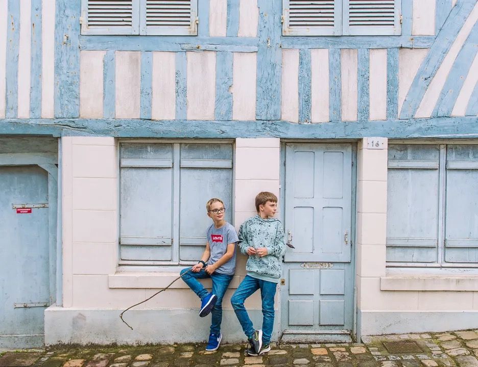 Two children sitting on a step outside a blue timber-framed building.